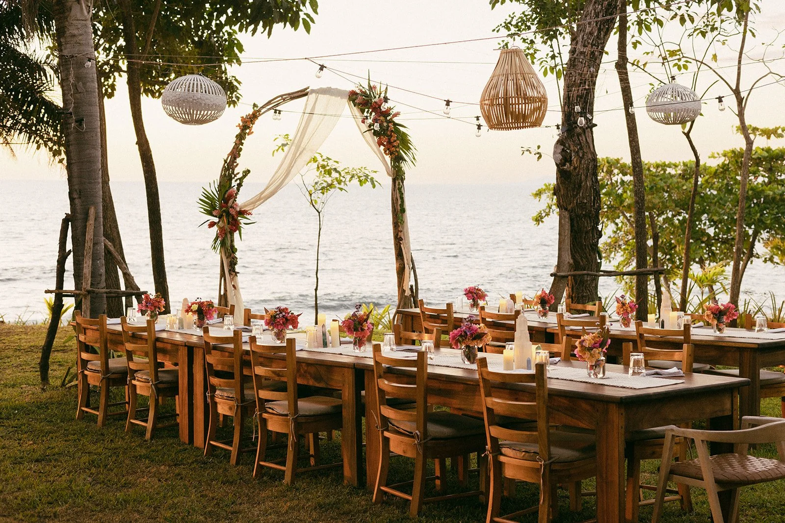 Outdoor wedding reception at Still Salty Escape in Nicaragua with tables set for dinner, tropical flowers, and a driftwood wedding arch overlooking the ocean
