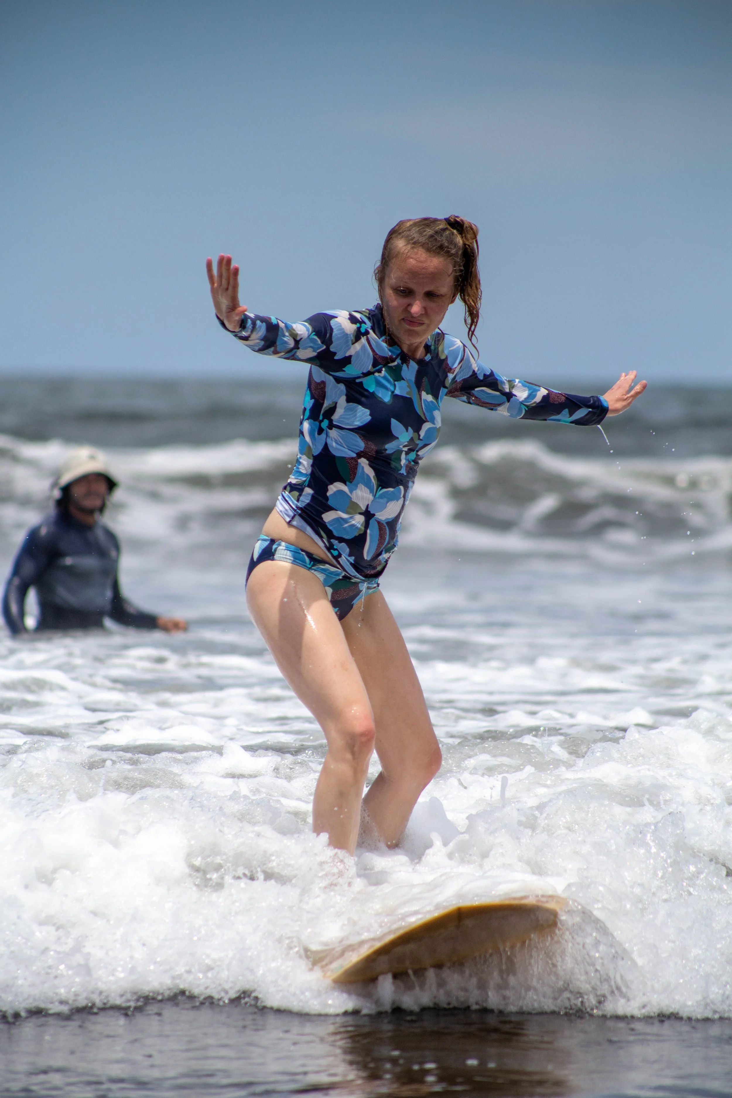 Surf student finding her balance on a wave with an instructor nearby at a learn to surf retreat in Nicaragua