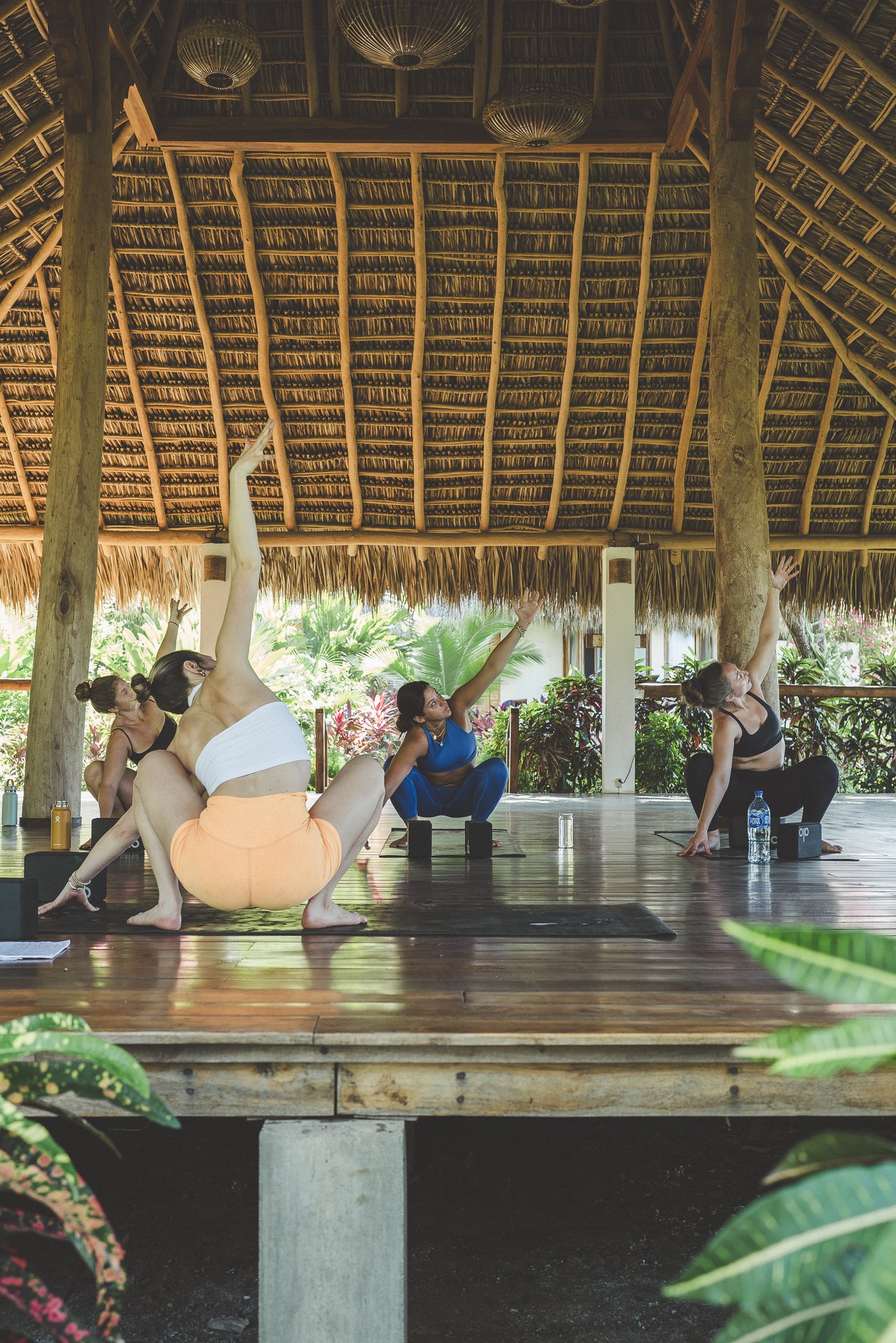 Retreat group in a malasana yoga pose during a yoga class in the thatched shala at Still Salty Escape surf and yoga retreat in Nicaragua