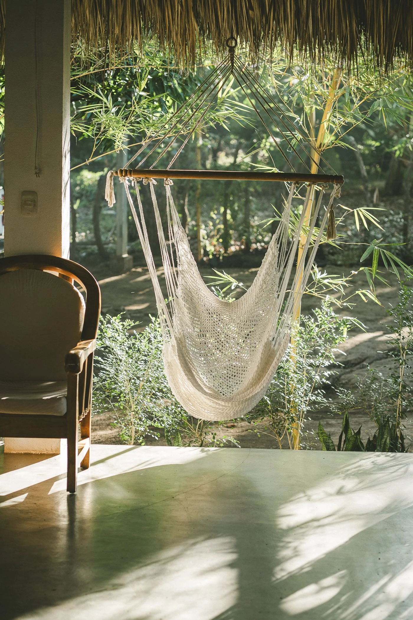 Woven hammock chair hanging on a shaded cabaña porch overlooking the gardens at a Nicaragua surf and yoga retreat