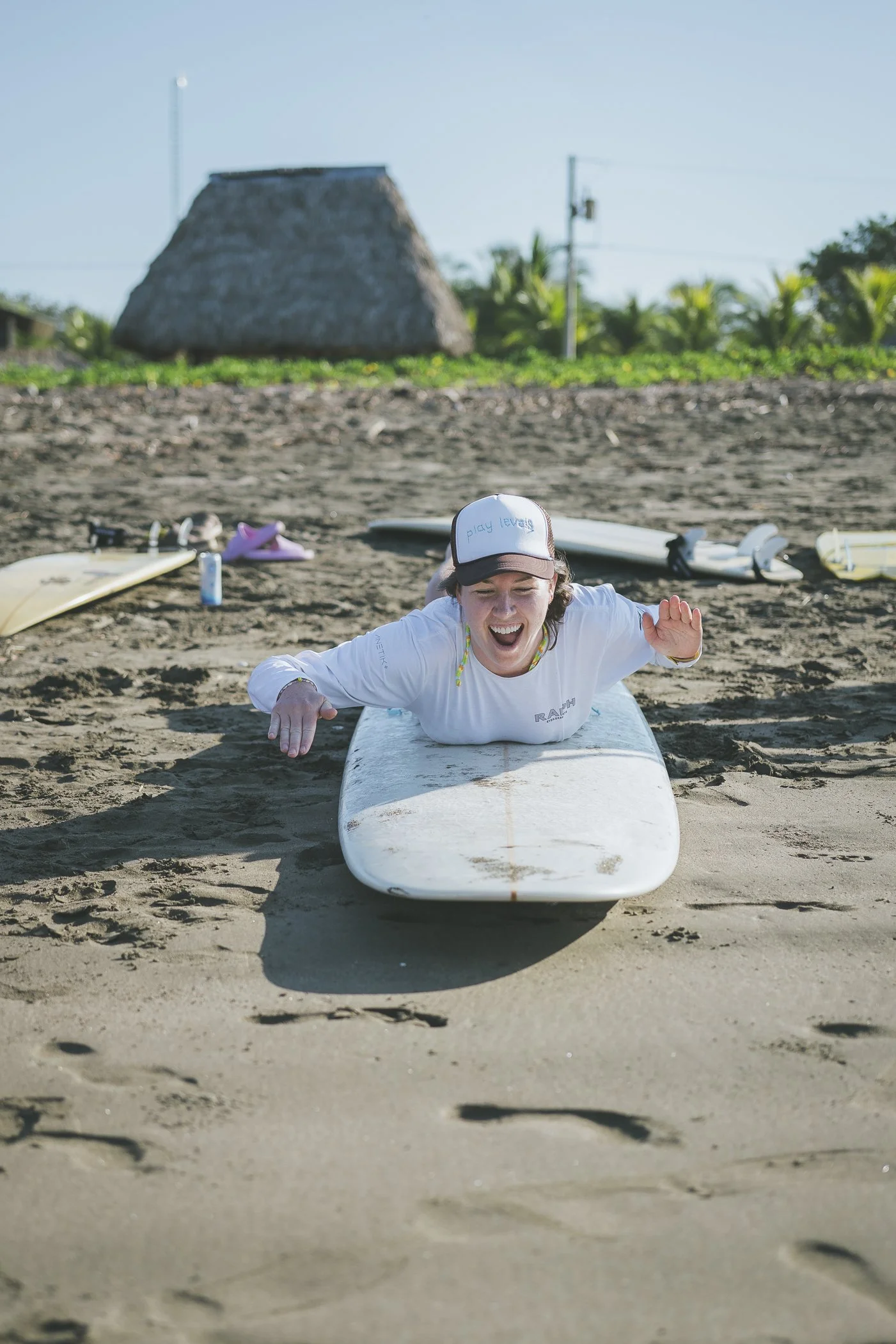 Surf student laughing during paddle practice on a longboard on the beach at a Nicaragua surf retreat