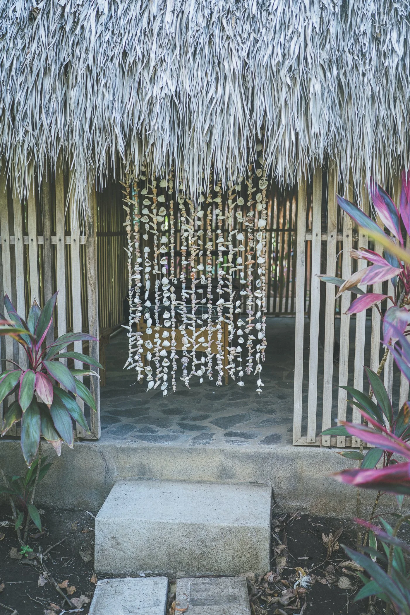 Entrance to a private massage shala with a handmade shell curtain and bamboo walls surrounded by gardens at Still Salty Escape Nicaragua