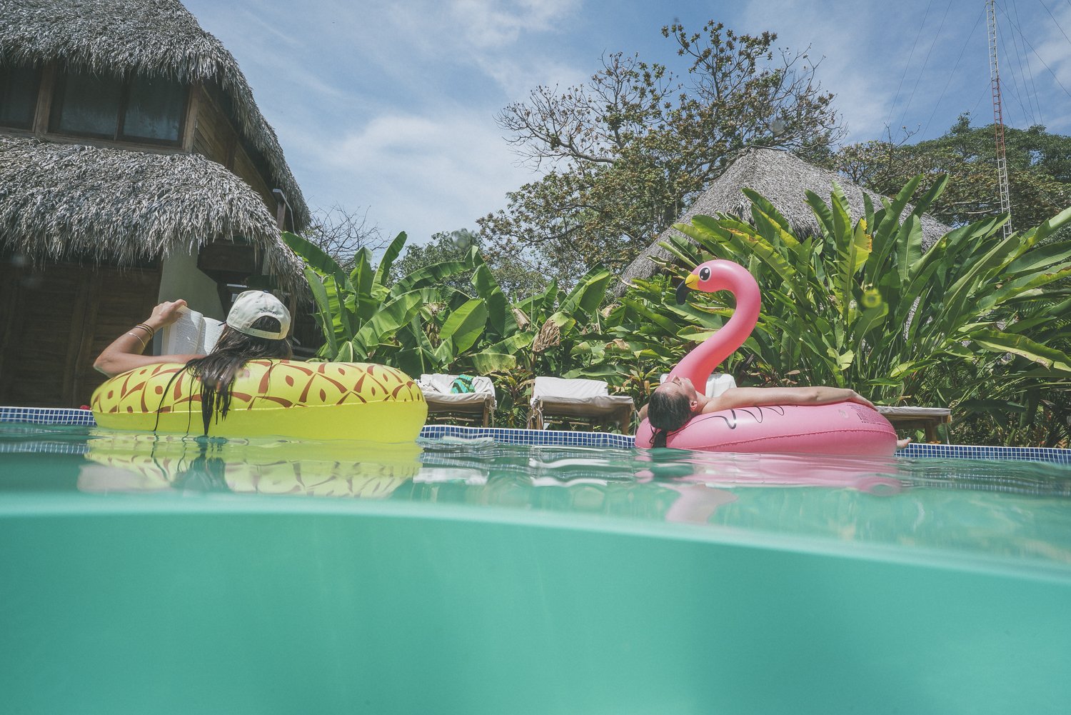 Retreat guests relaxing on pool floats beside thatched cabanas at a yoga retreat in Nicaragua
