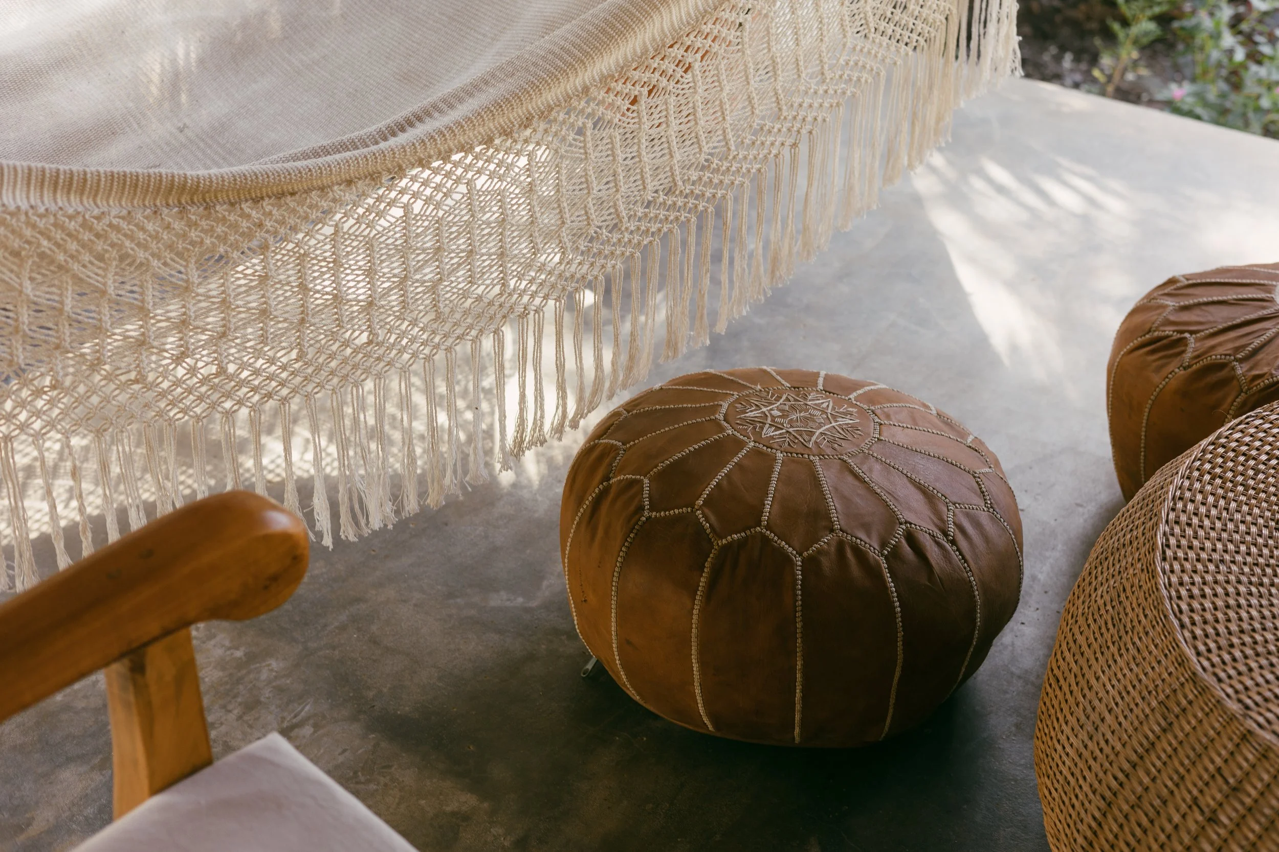 Woven hammock and leather poufs on a shaded patio framed by tropical gardens at a Nicaragua surf and yoga retreat