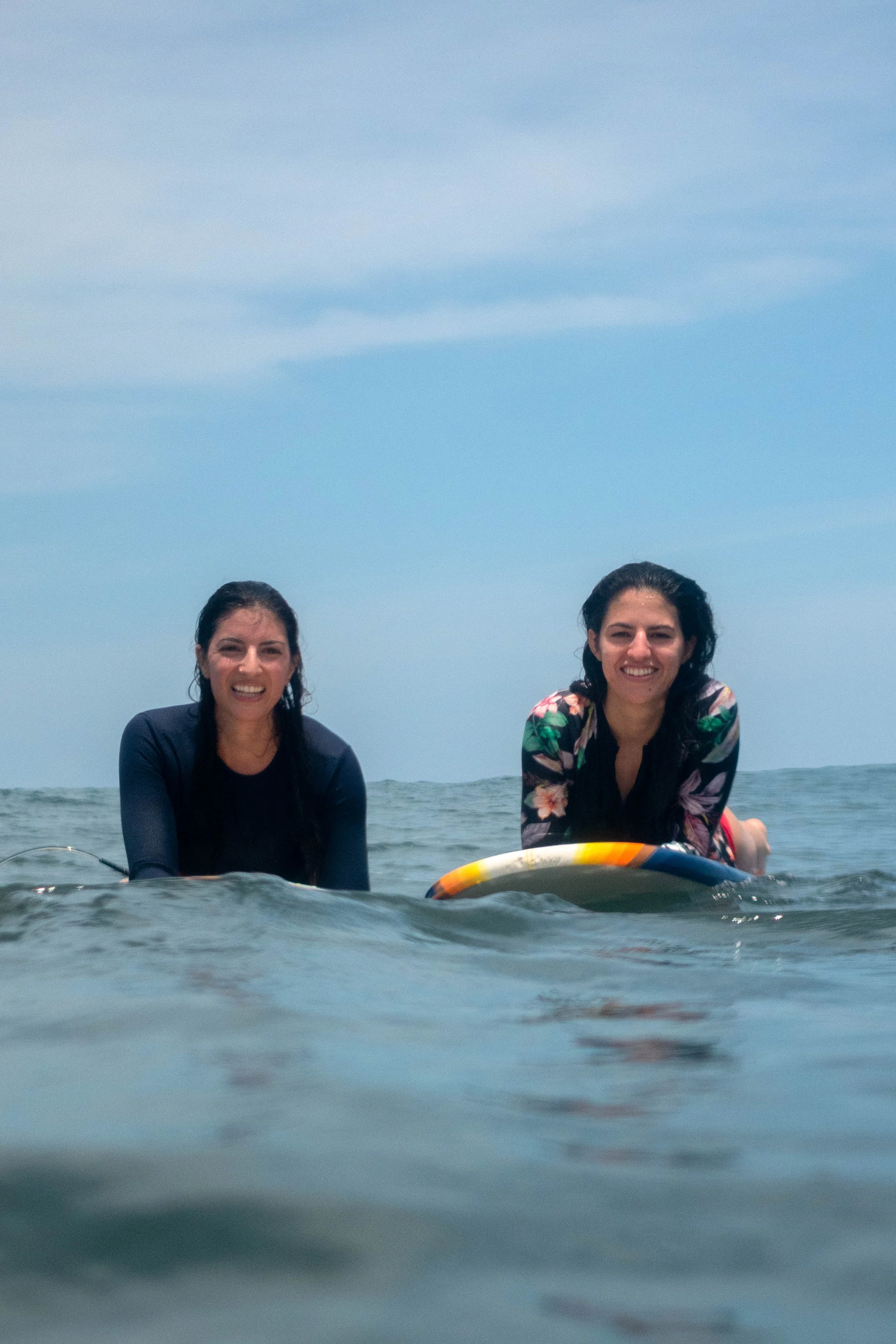 Two women smiling on their surfboards during a surf lesson in Nicaragua, geared up for their surf trip