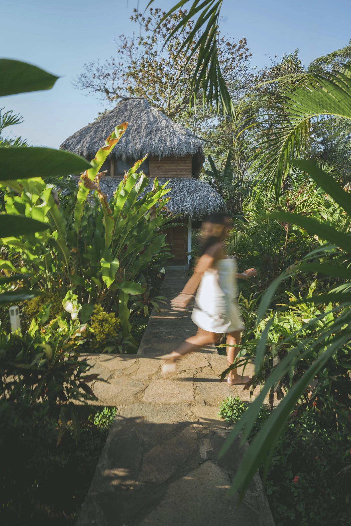 Guest walking a stone path through tropical gardens to a thatched-roof cabana at Still Salty Escape retreat in Nicaragua