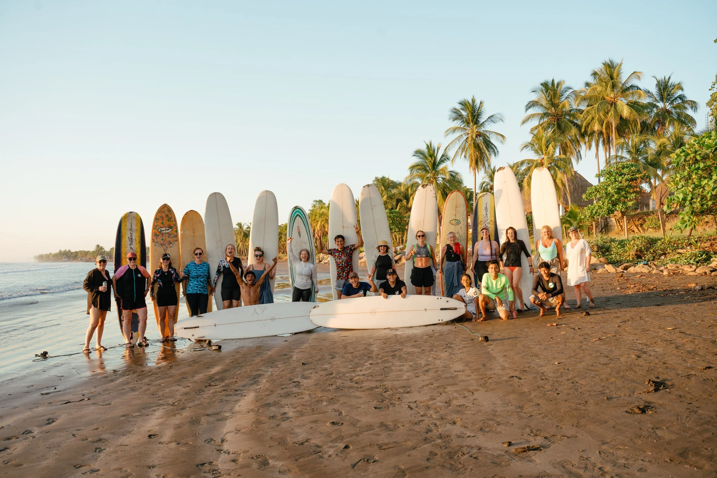 Large surf retreat group posing with longboards on the beach at sunset after a surf session in Nicaragua