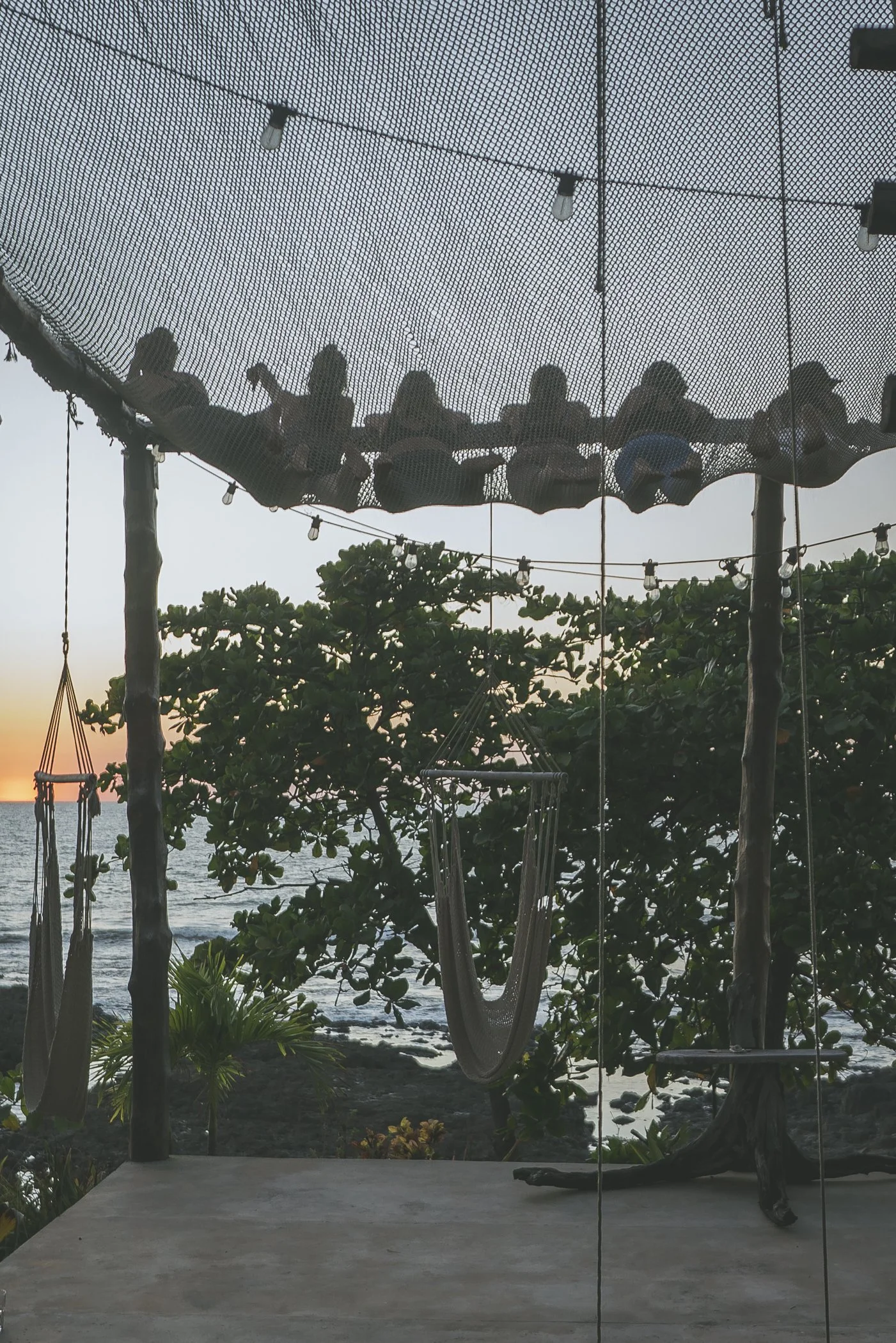 Handwoven hammock chairs and string lights beneath the oceanfront net hammock at sunset at Still Salty Escape Nicaragua