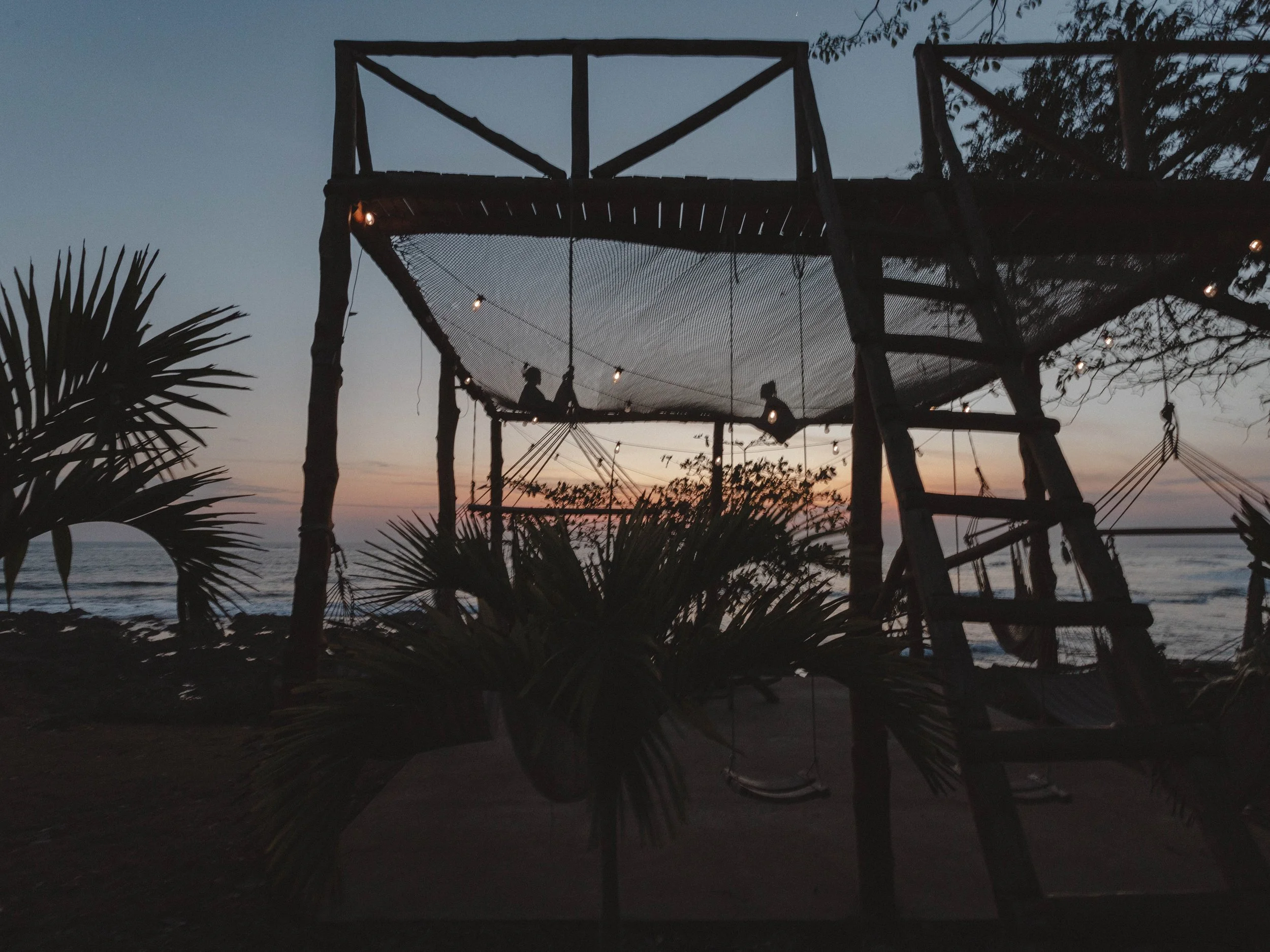 Guests relaxing on the giant oceanfront net hammock under string lights at dusk at Still Salty Escape in Nicaragua