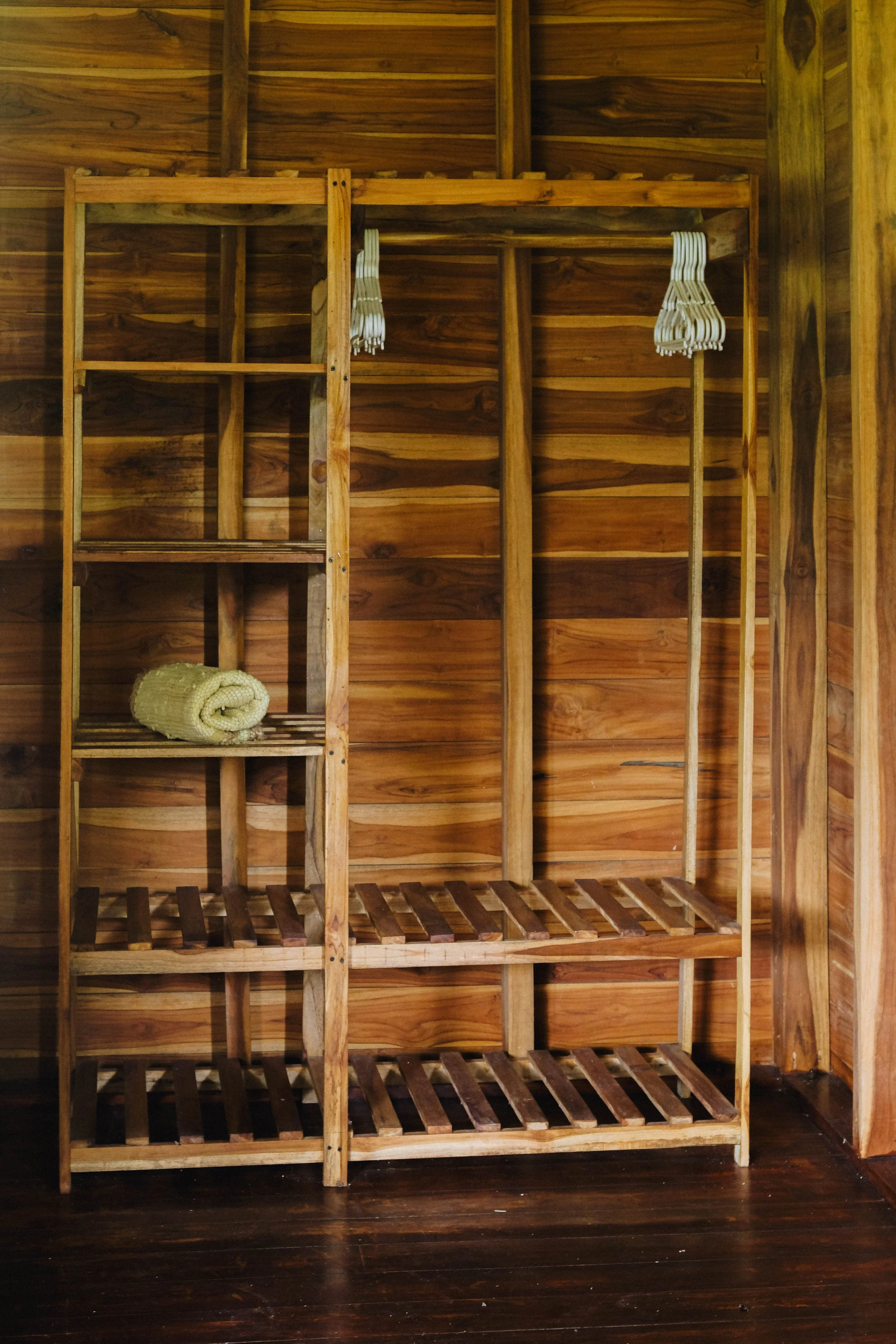 Open teak clothing storage with hangers and folded towels in a cabaña room at Still Salty Escape surf and yoga retreat in Nicaragua