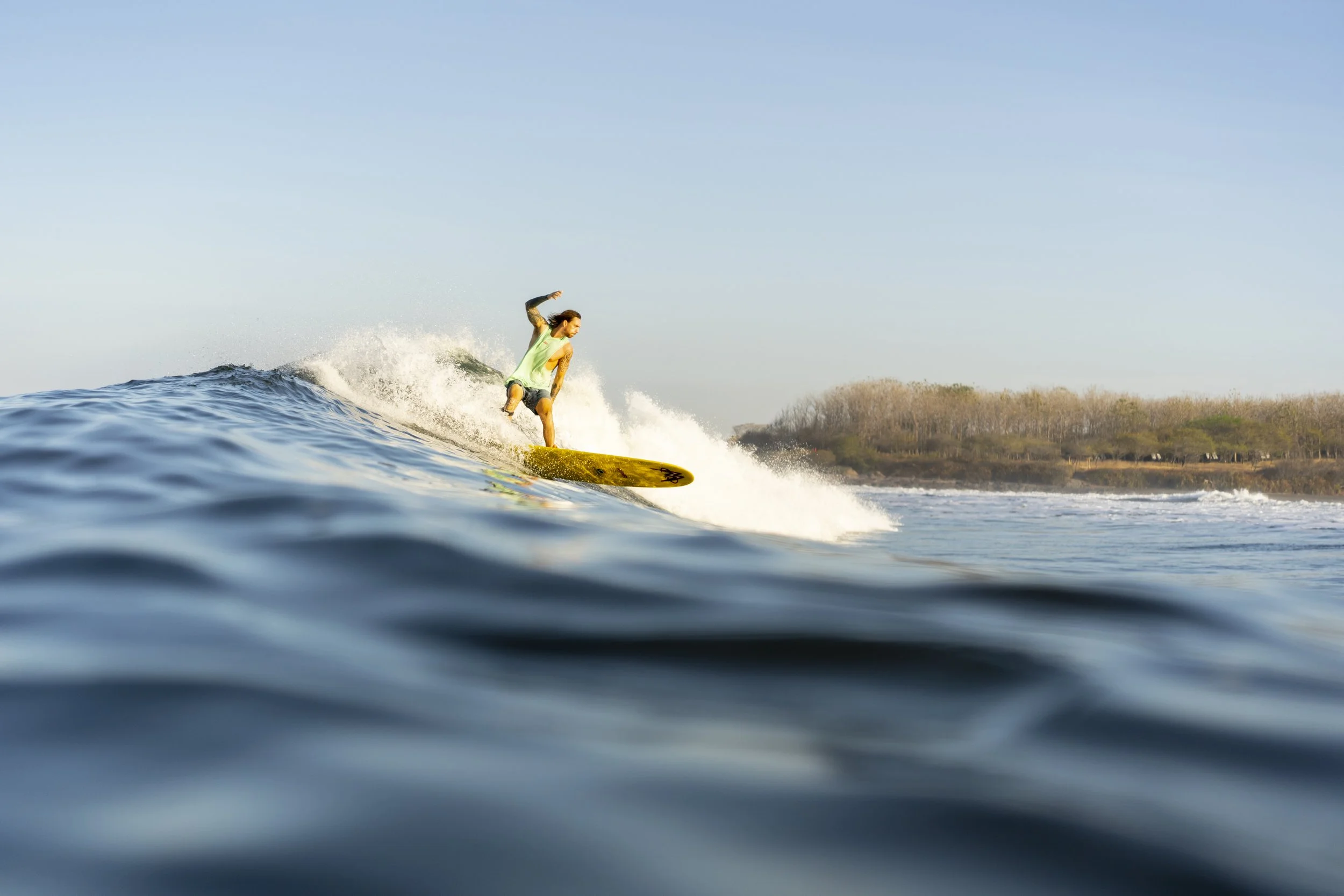 Experienced surfer riding a peeling green wave on a longboard along the coast at a surf retreat in Nicaragua