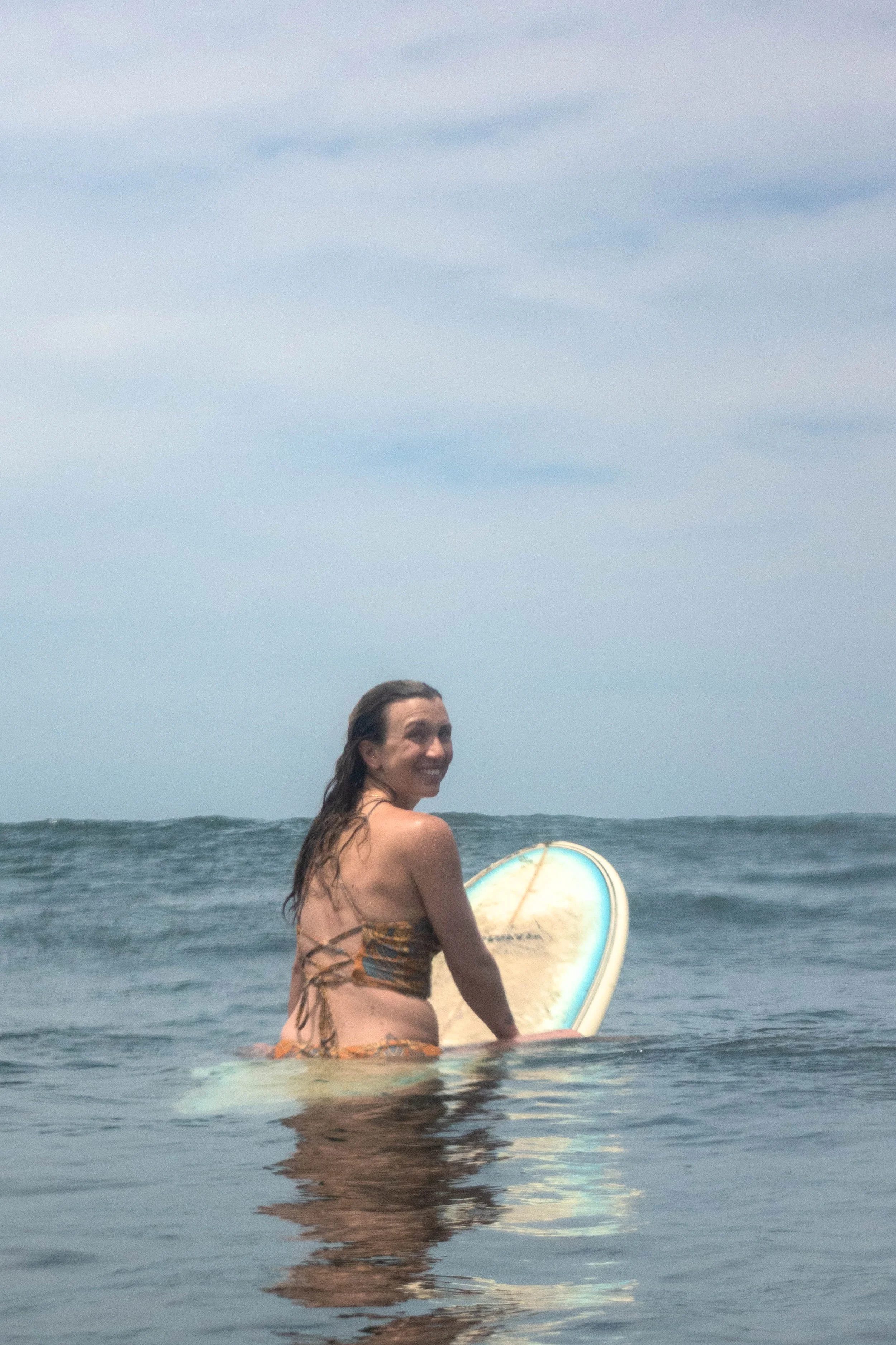 Happy surfer sitting on her longboard in the lineup during a surf retreat in Nicaragua