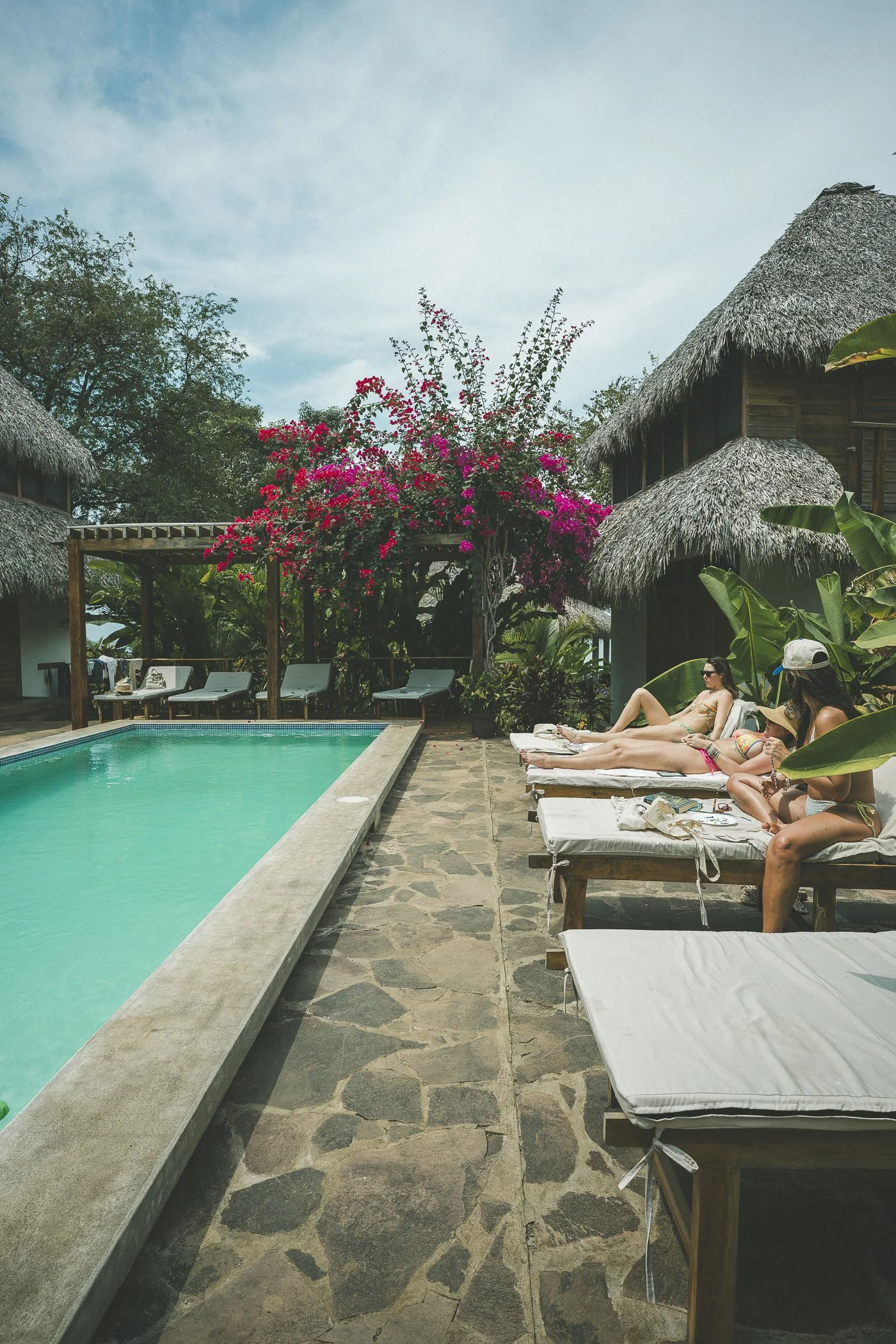 Guests relaxing on shaded loungers beside the lap pool and bougainvillea at a surf and yoga retreat in Nicaragua