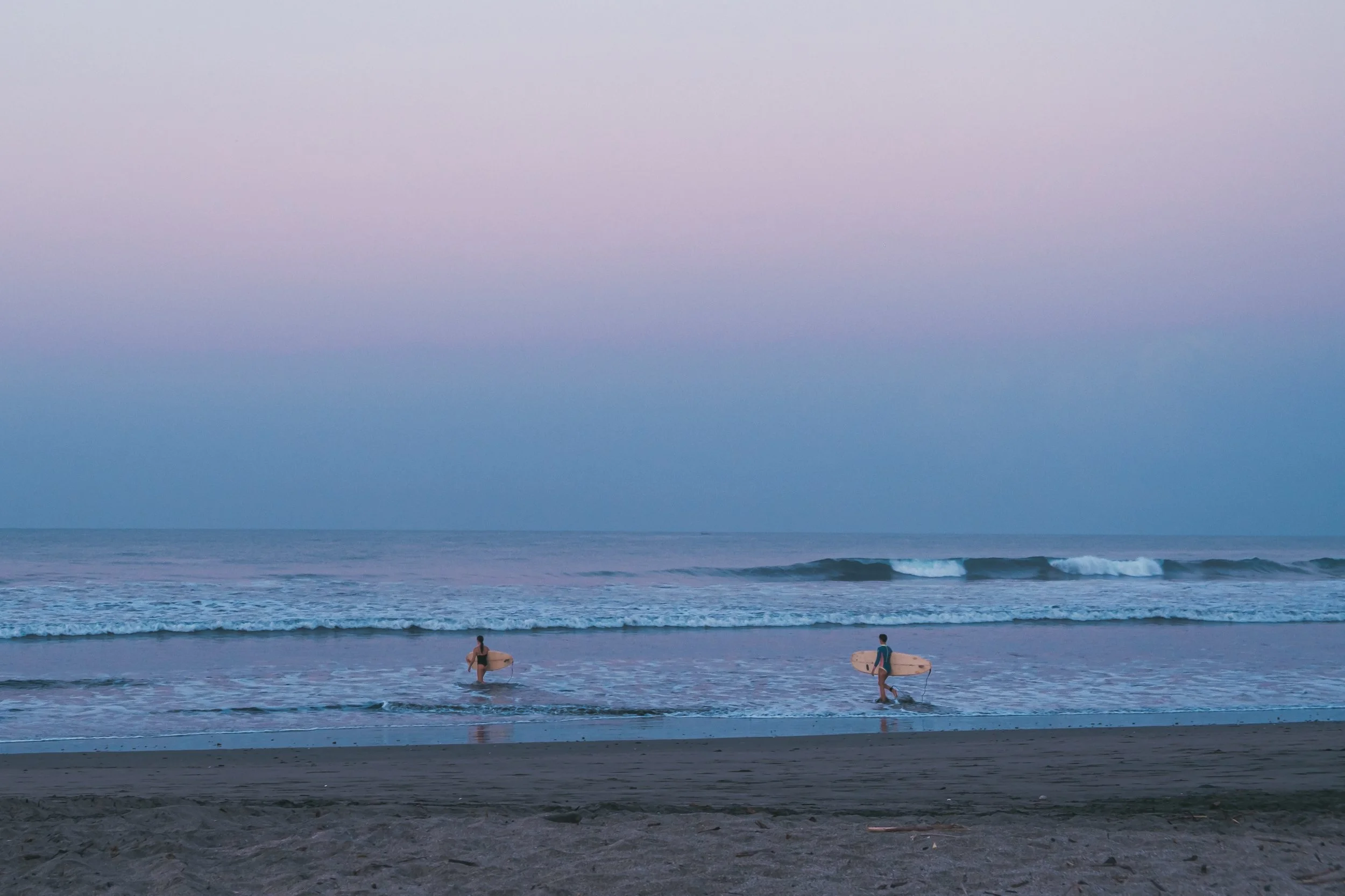 Two surfers walking into the uncrowded waves at sunrise with their boards at a Nicaragua surf camp