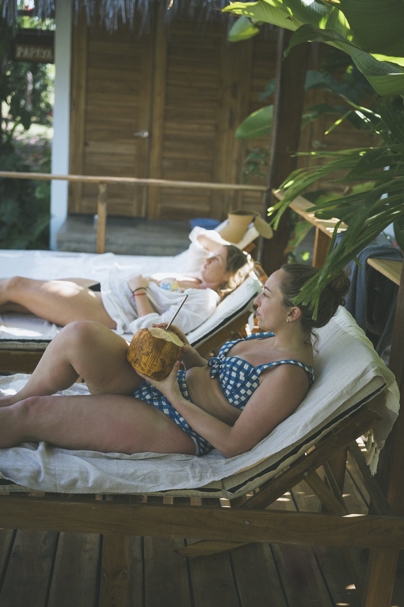 Two guests resting on loungers on a shaded cabaña porch with a fresh coconut at Still Salty Escape retreat in Nicaragua