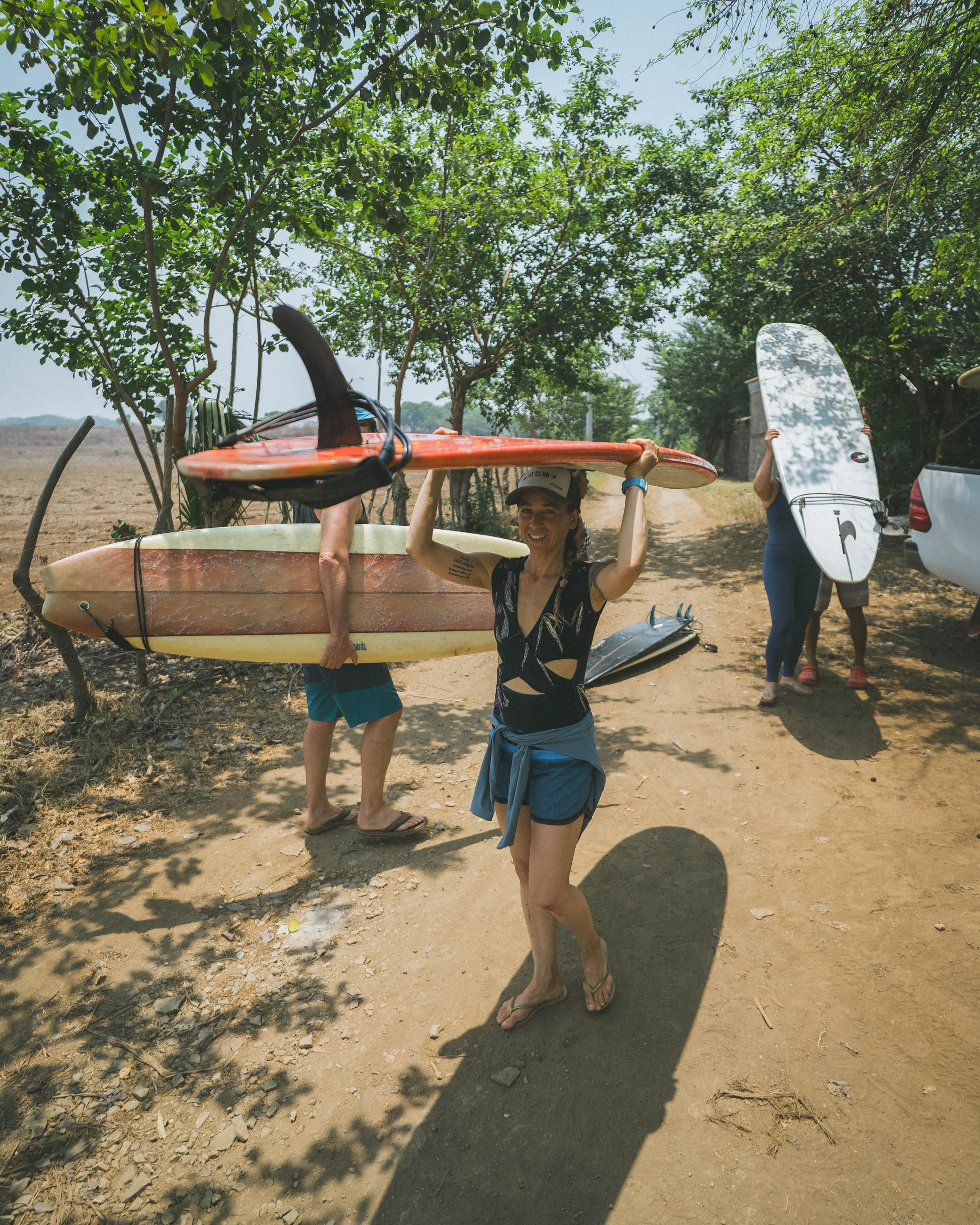 Surfers carrying boards down a tree-lined path to the beach at Still Salty Escape surf camp in Nicaragua