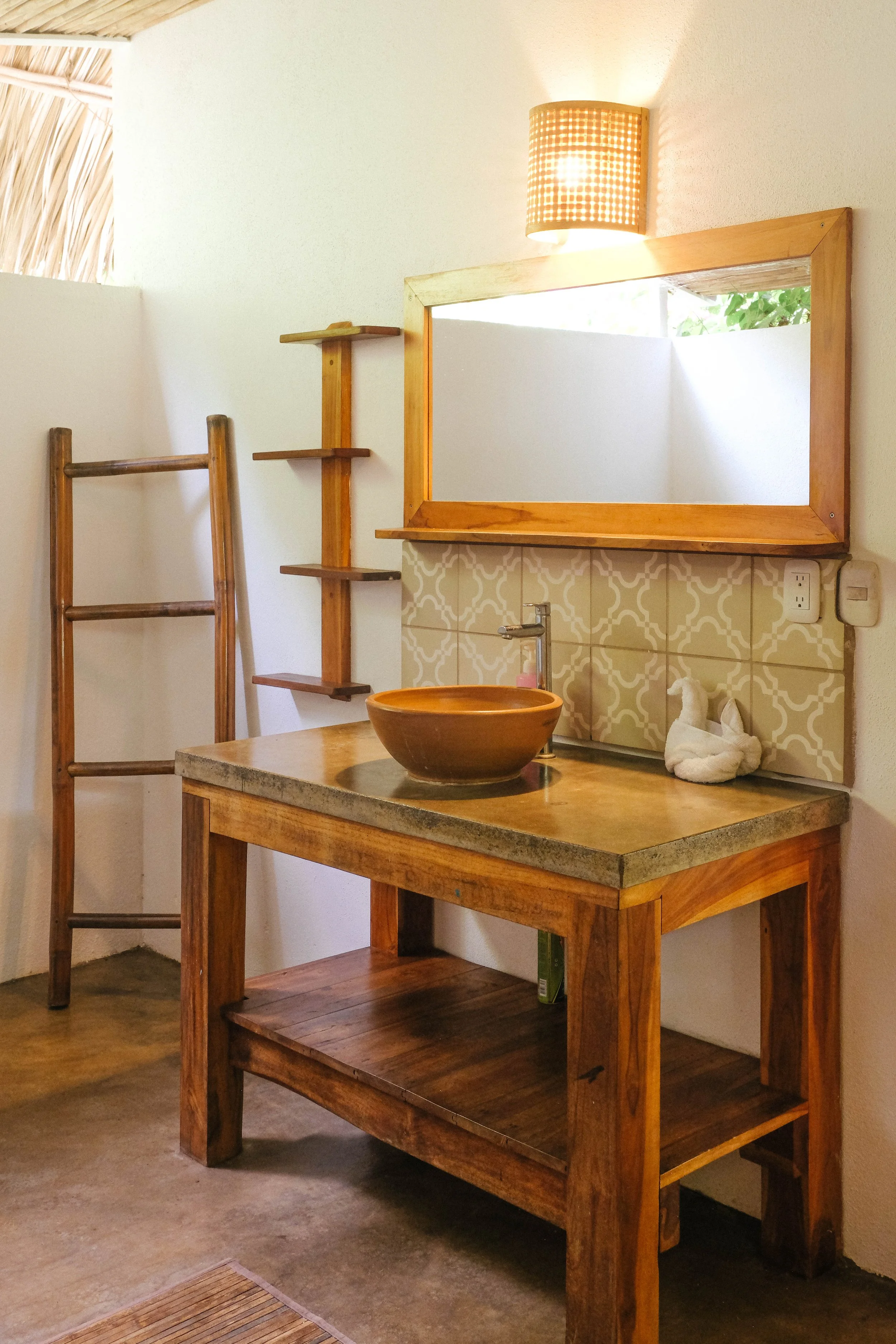 Covered outdoor bathroom with a wood vanity, clay bowl sink, and bamboo towel ladder in a downstairs cabaña at a Nicaragua surf and yoga retreat
