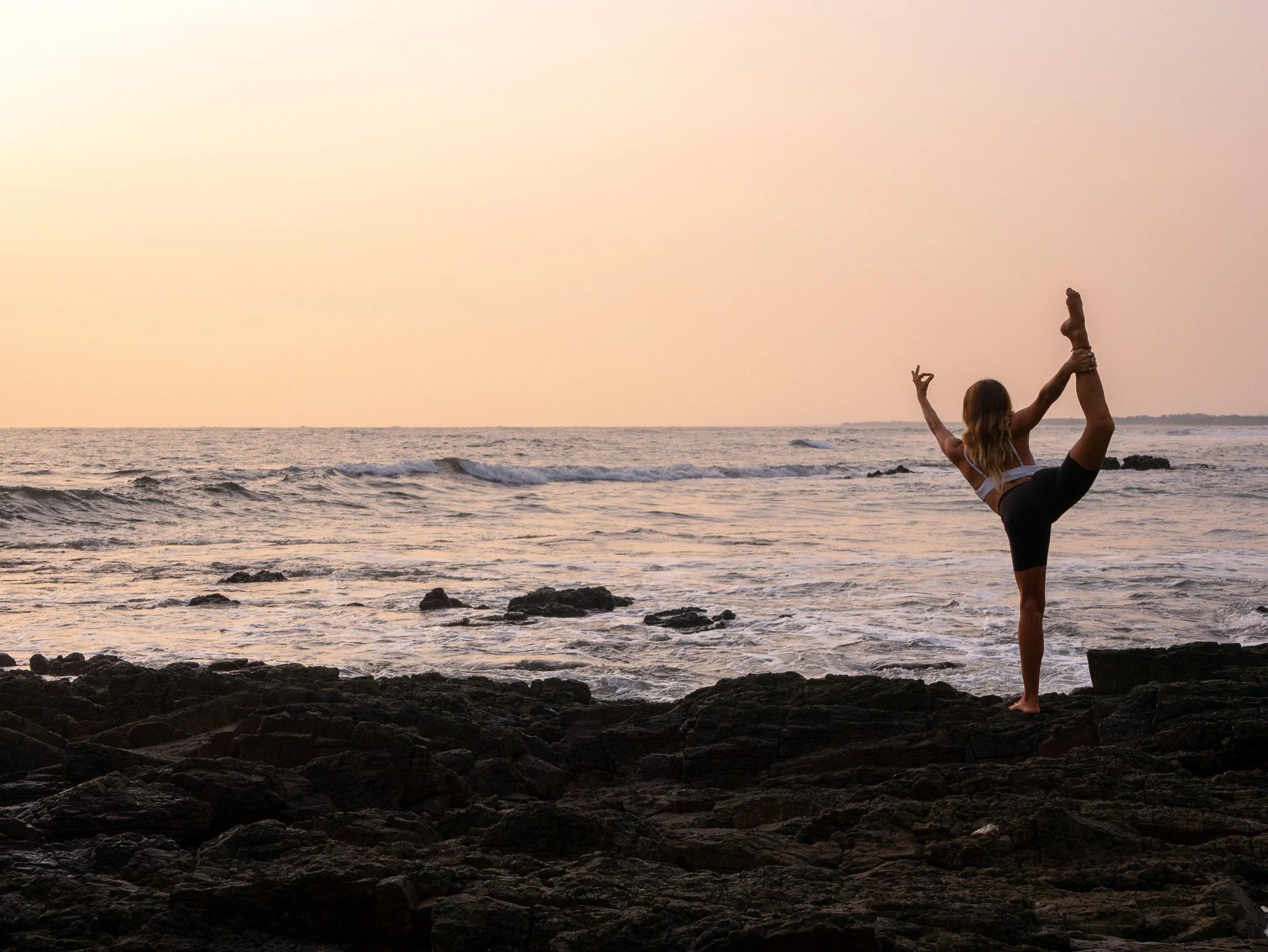 Yoga teacher in dancer's pose on the rocks above the Pacific at sunset in Nicaragua