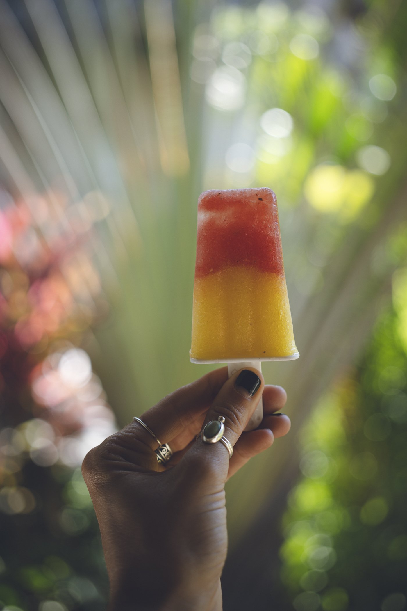 Hand holding a two-layer watermelon and mango fruit popsicle in the garden at Still Salty Escape surf and yoga retreat in Nicaragua