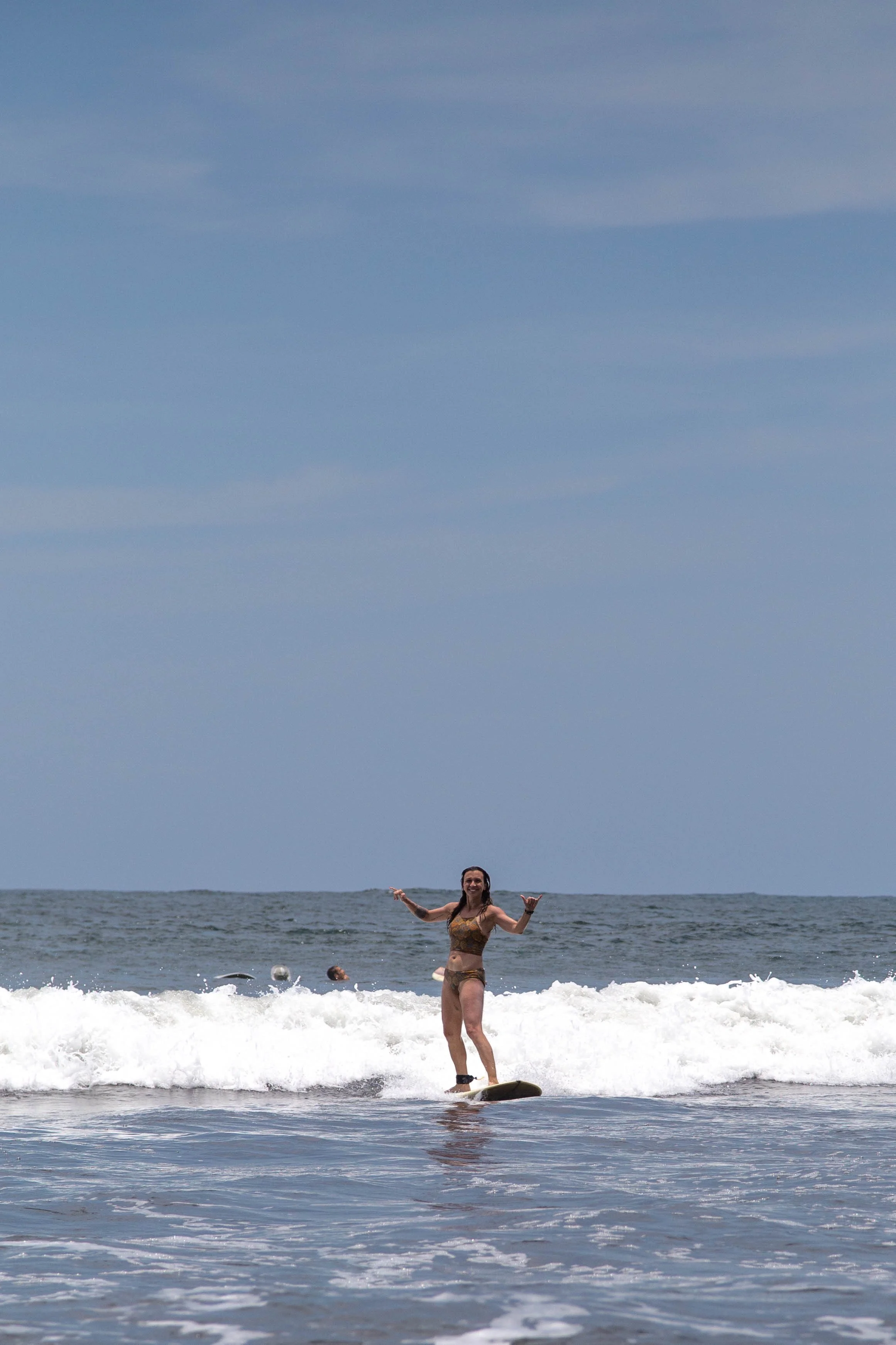 Beginner surfer riding a wave and throwing shakas during a learn to surf lesson in Nicaragua