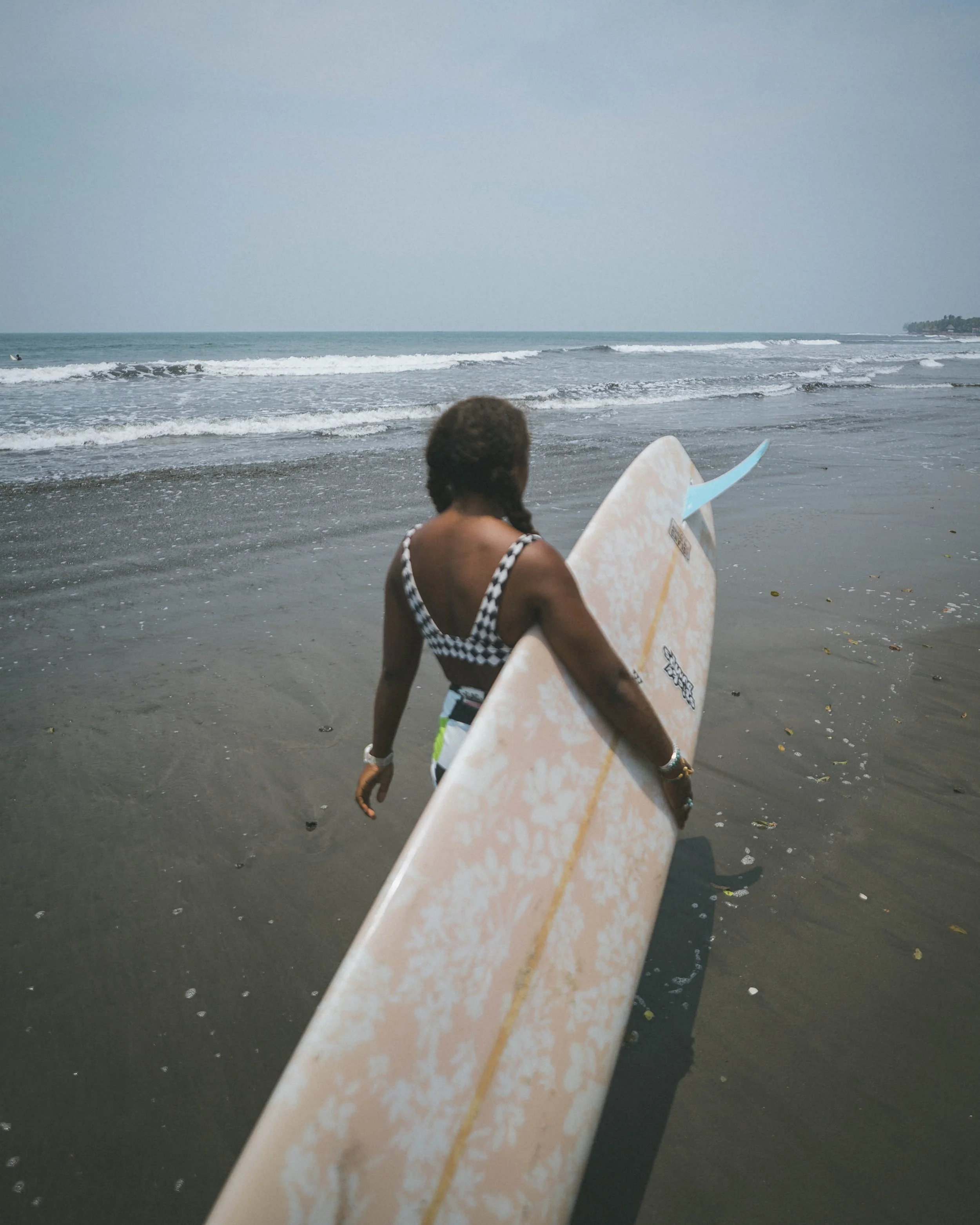 woman walking with a longboard to the waves at a surf camp in Nicaragua