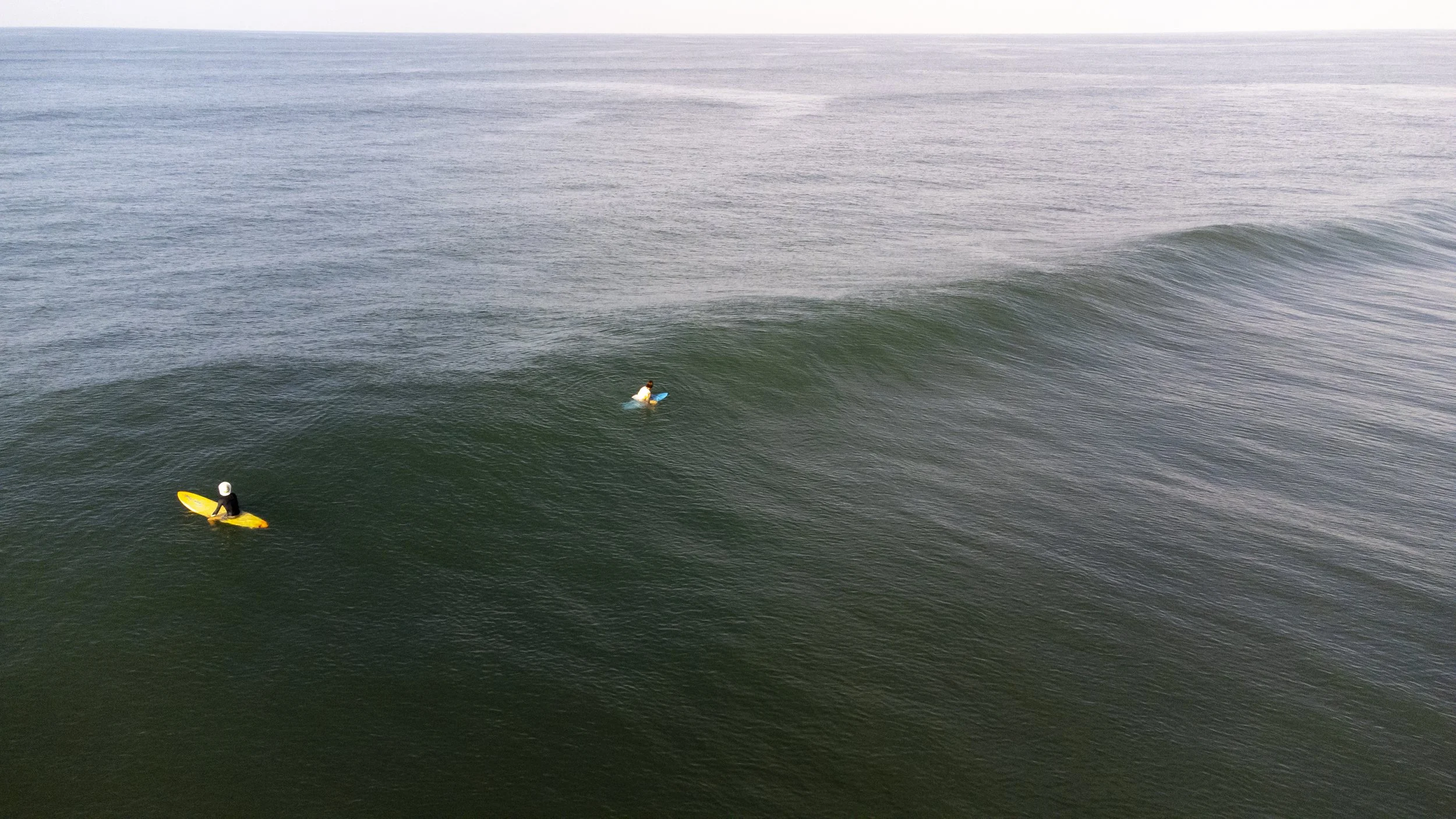 Two surfers paddling out in clear water on a surf and yoga retreat in Nicaragua, overhead drone view