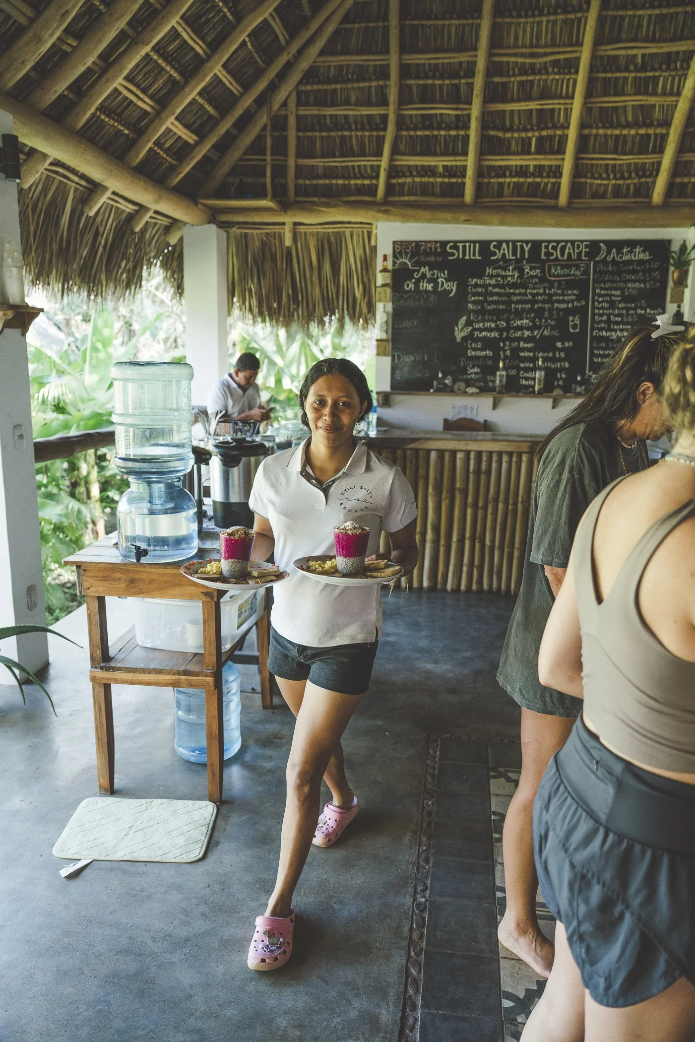 Team member carrying two breakfast plates with dragon fruit chia and eggs past the menu board at Still Salty Escape Nicaragua