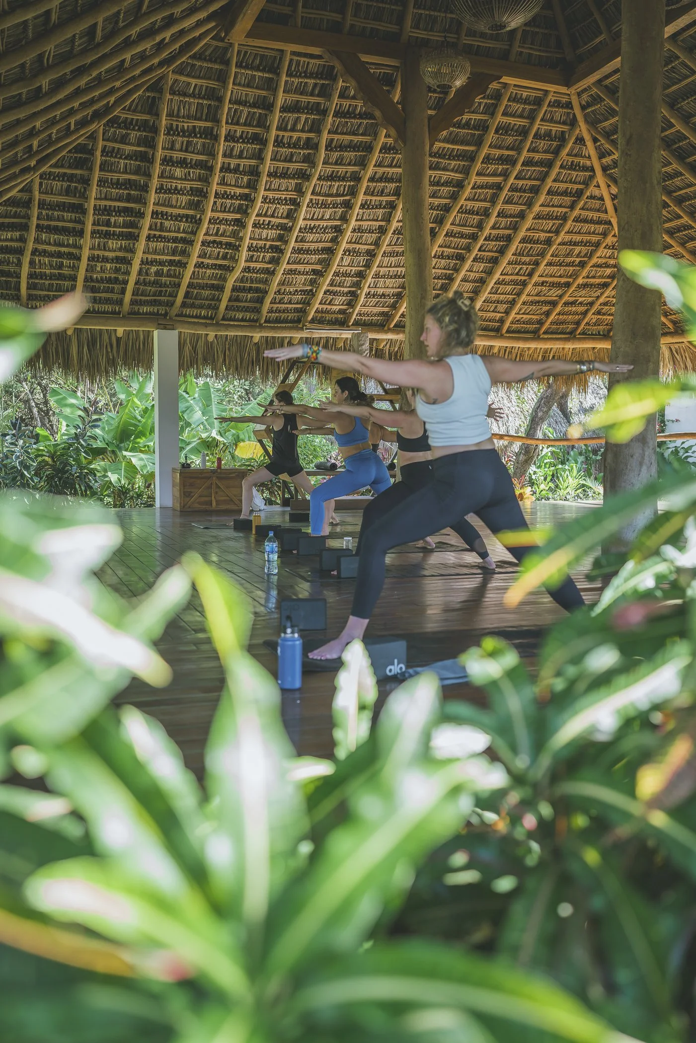 Yoga retreat group in Warrior II during a practice in the open-air shala framed by gardens at Still Salty Escape Nicaragua