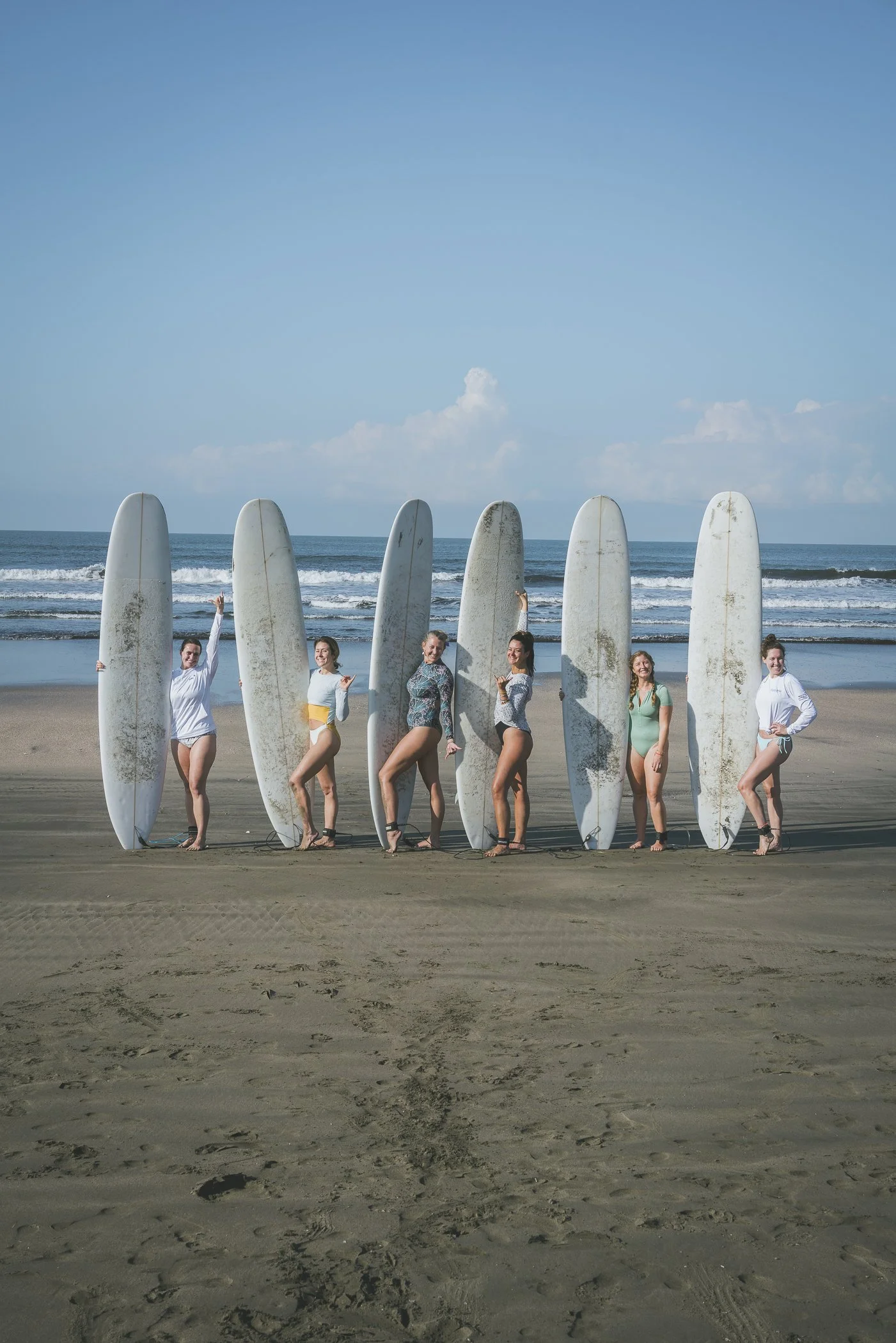 Group of women posing behind their longboards on the beach after a session at a surf and yoga retreat in Nicaragua