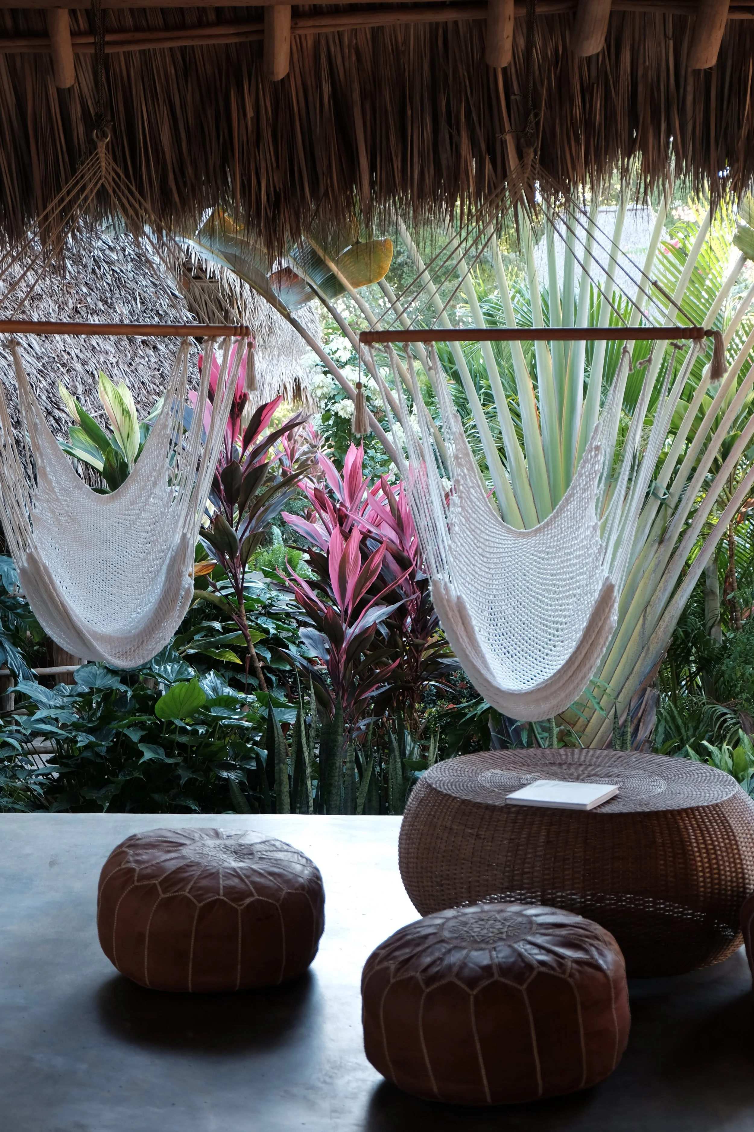 Two hanging hammock chairs and leather poufs on a shaded patio overlooking tropical gardens at a Nicaragua surf and yoga retreat