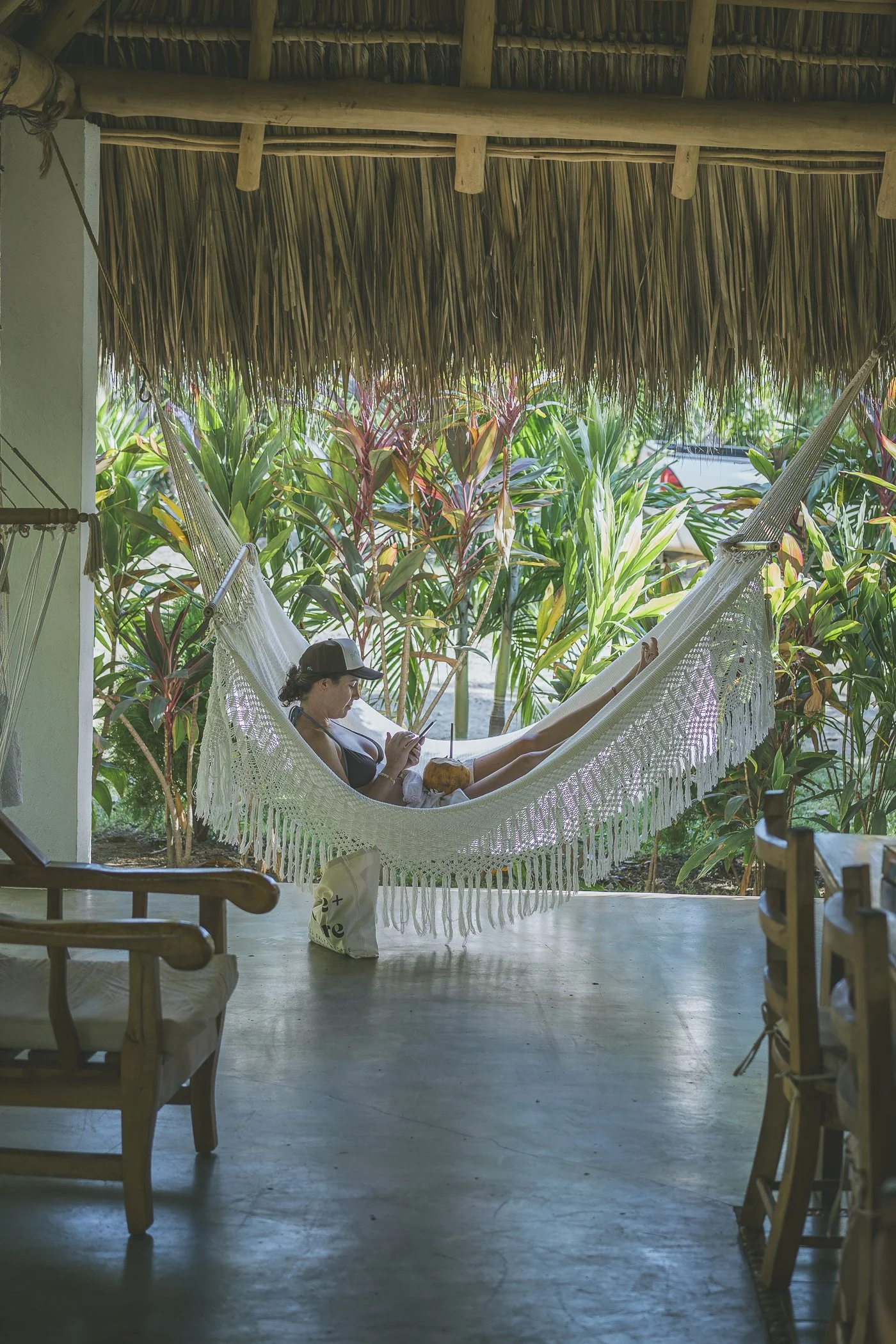 Guest relaxing in a fringed hammock with a coconut overlooking tropical gardens at a Nicaragua surf and yoga retreat