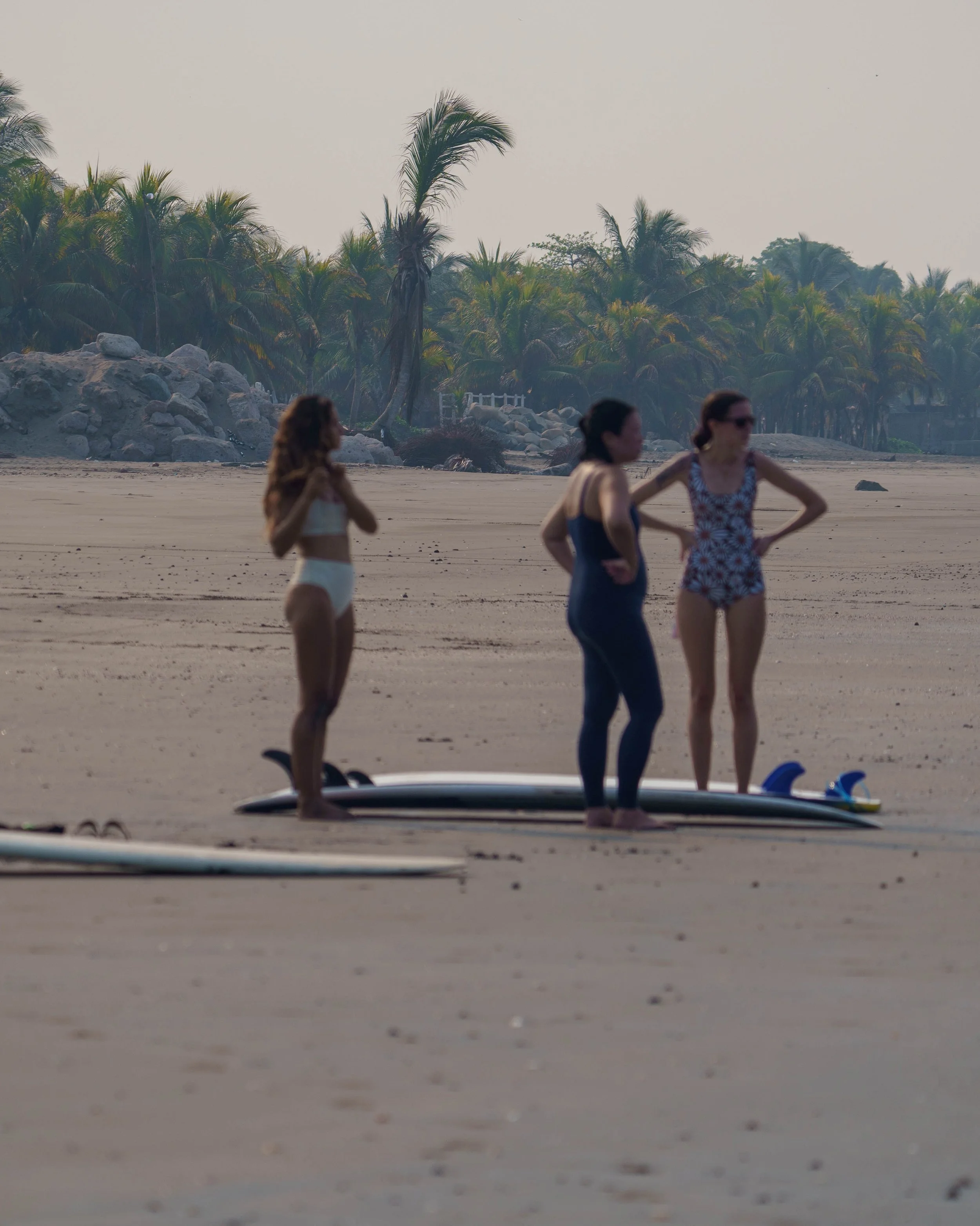 Three  surf retreat guests with longboards on the empty beach at dawn during a surf retreat in Nicaragua