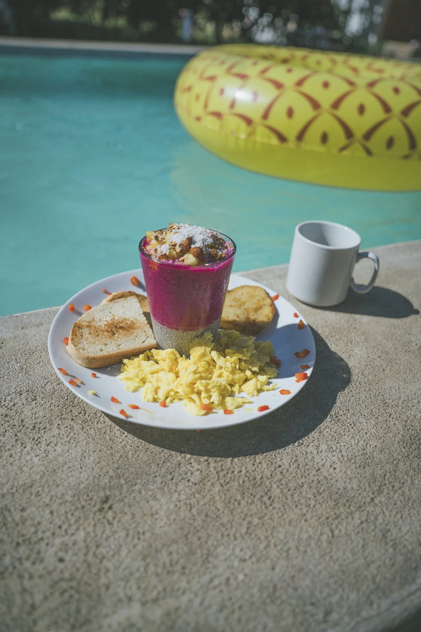 Poolside breakfast of dragon fruit chia, scrambled eggs, and toast beside a pineapple float at Still Salty Escape Nicaragua