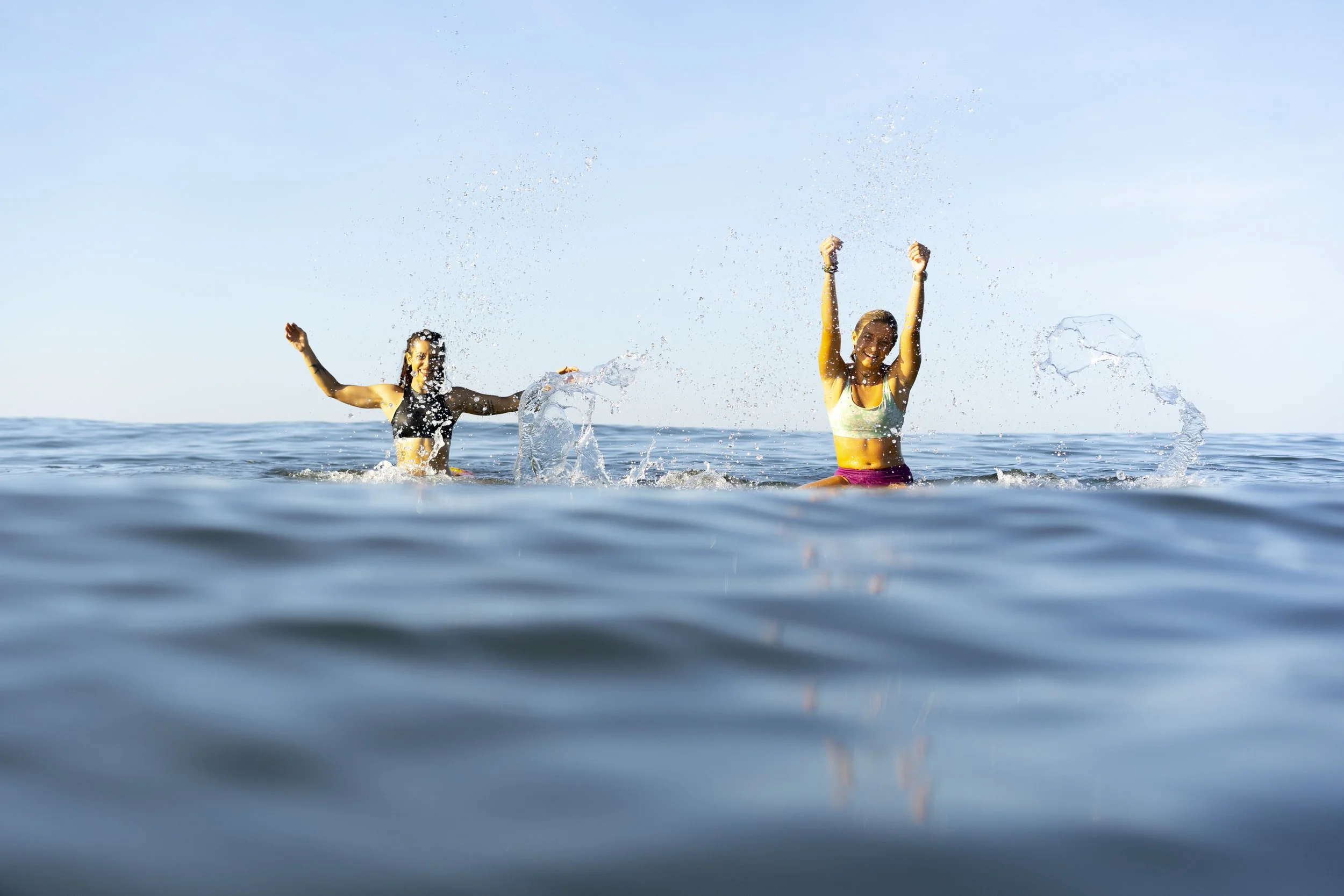 Two women laughing and splashing in the ocean during a small-group surf retreat in Nicaragua