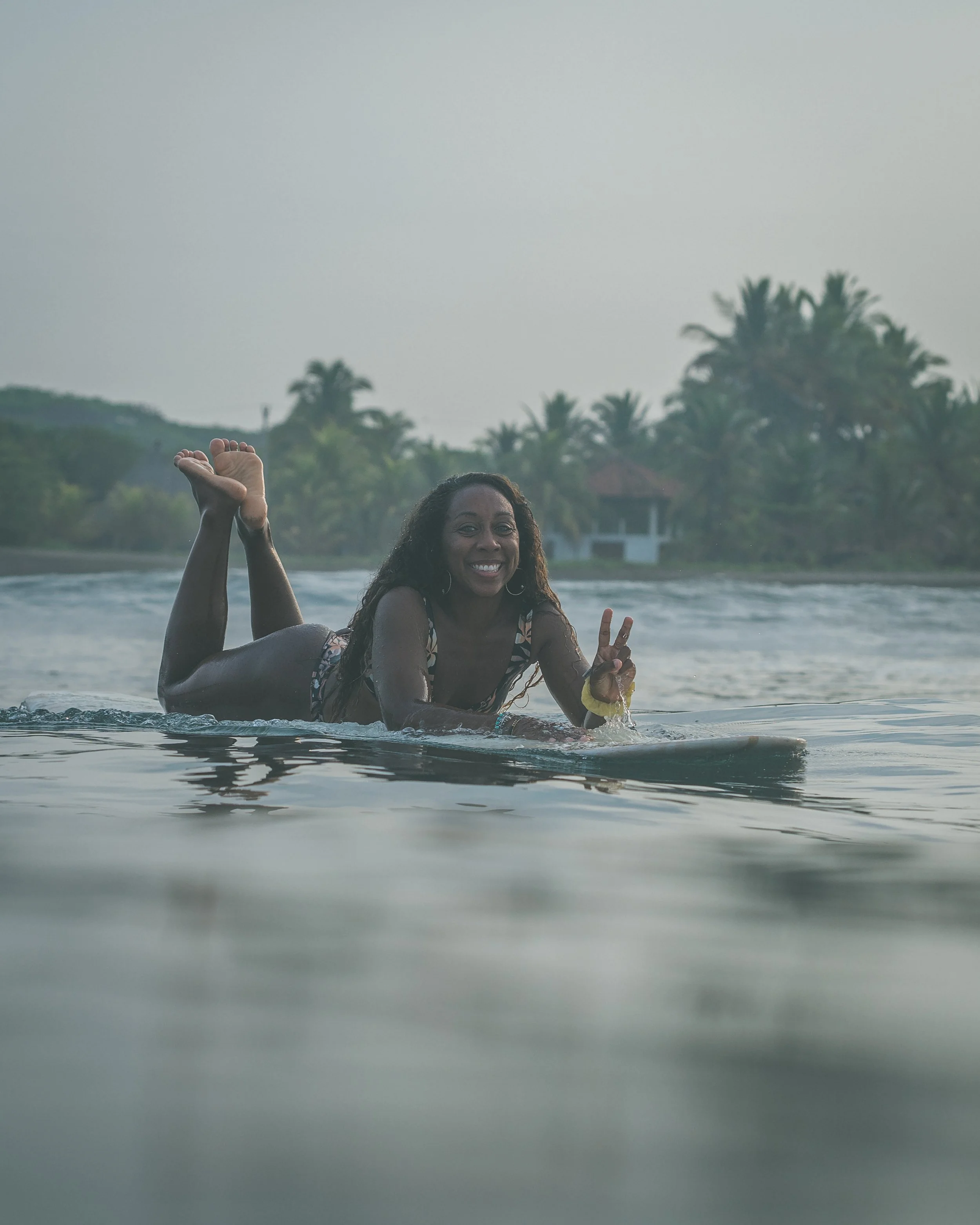 Smiling surfer paddling a longboard in warm water at a surf retreat in Nicaragua