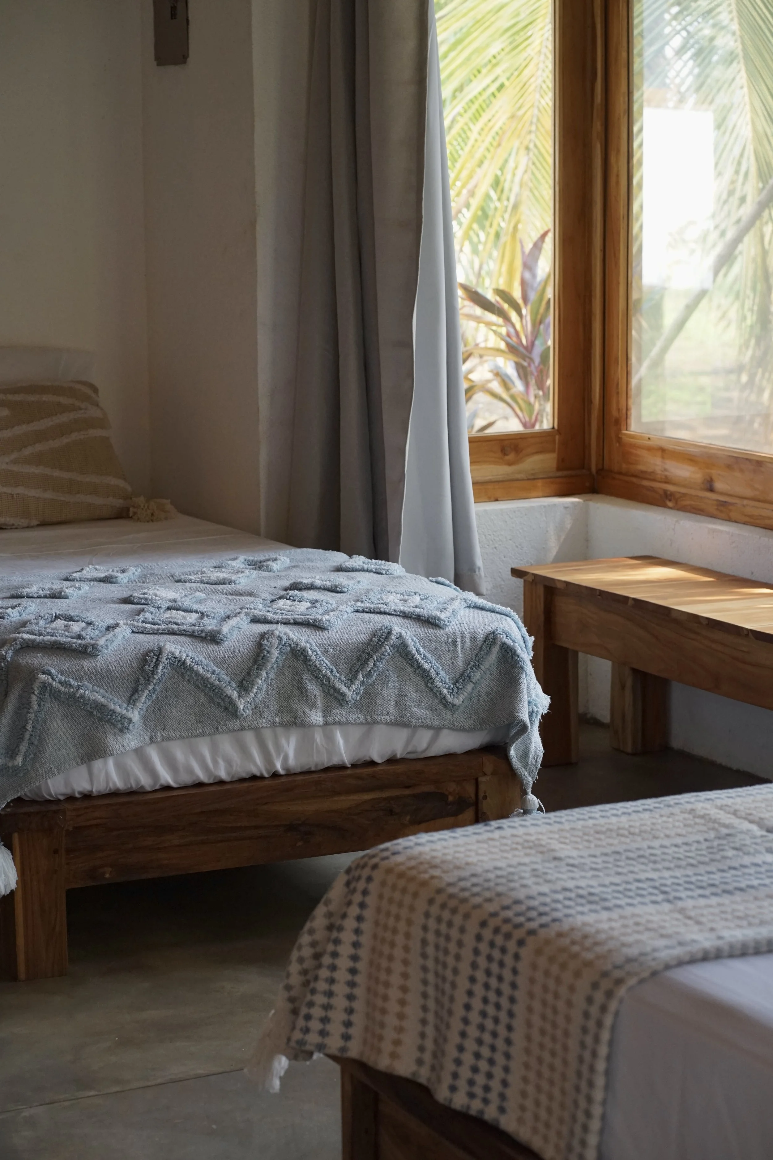 Single beds dressed in handmade textured blankets in a downstairs cabaña room at Still Salty Escape surf and yoga retreat in Nicaragua