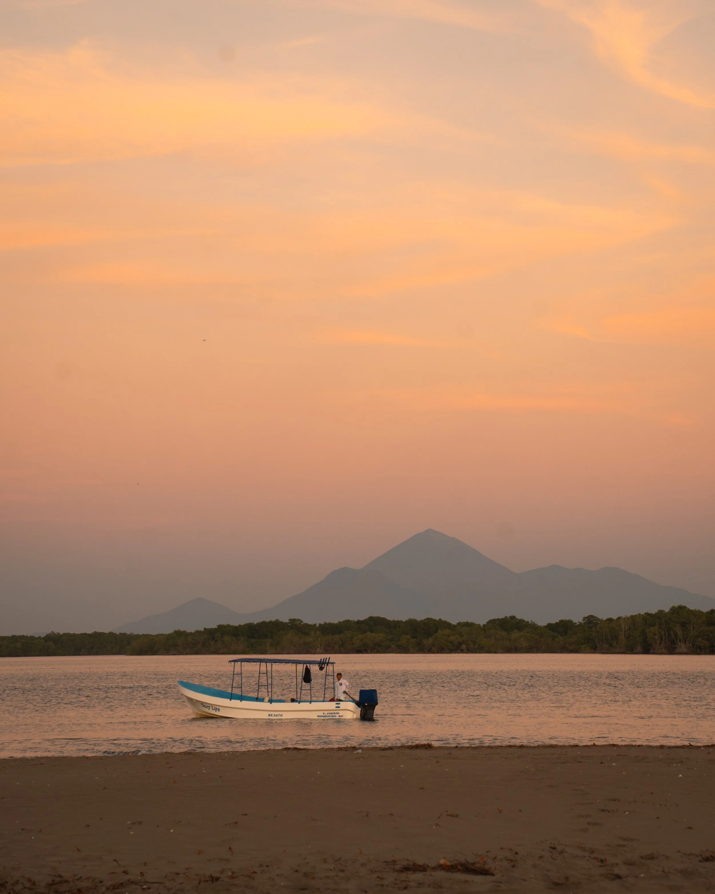 Panga boat on a calm estuary with a volcano behind at sunset near Still Salty Escape in Nicaragua