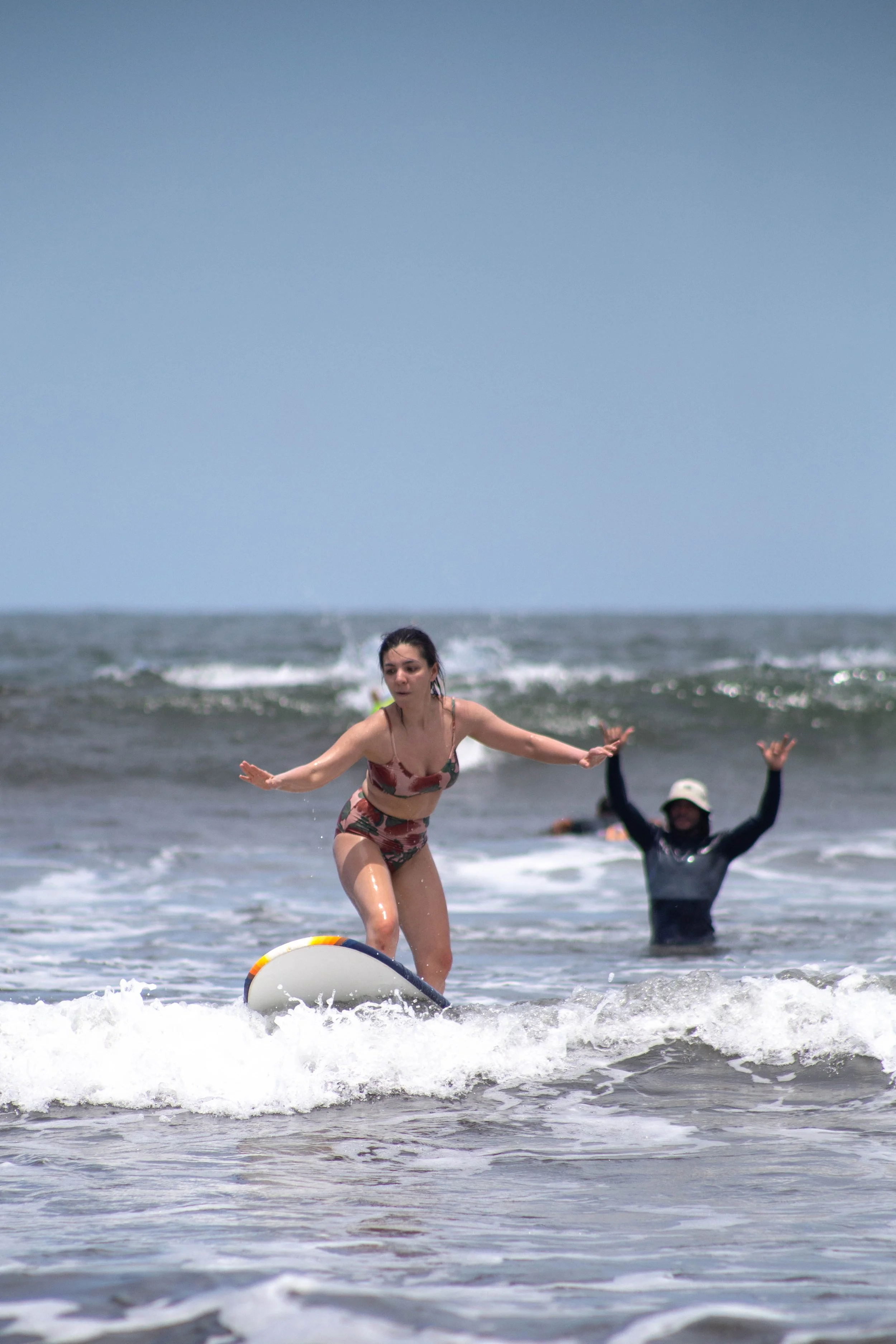 Beginner surfer riding whitewater on a foam board while an instructor cheers at a learn to surf camp in Nicaragua