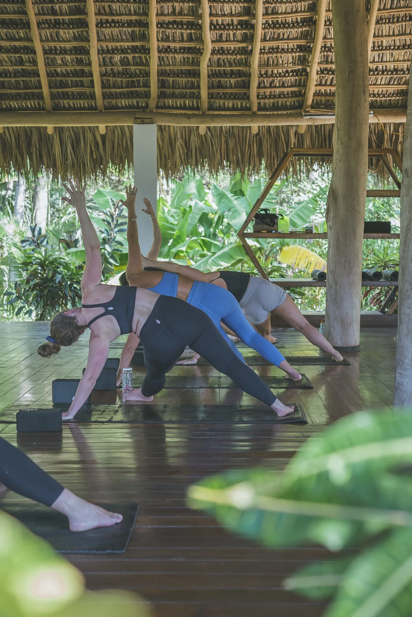 Group of guests in a side-angle yoga pose under the thatched roof of the open-air ocean-view shala at a Nicaragua surf and yoga retreat