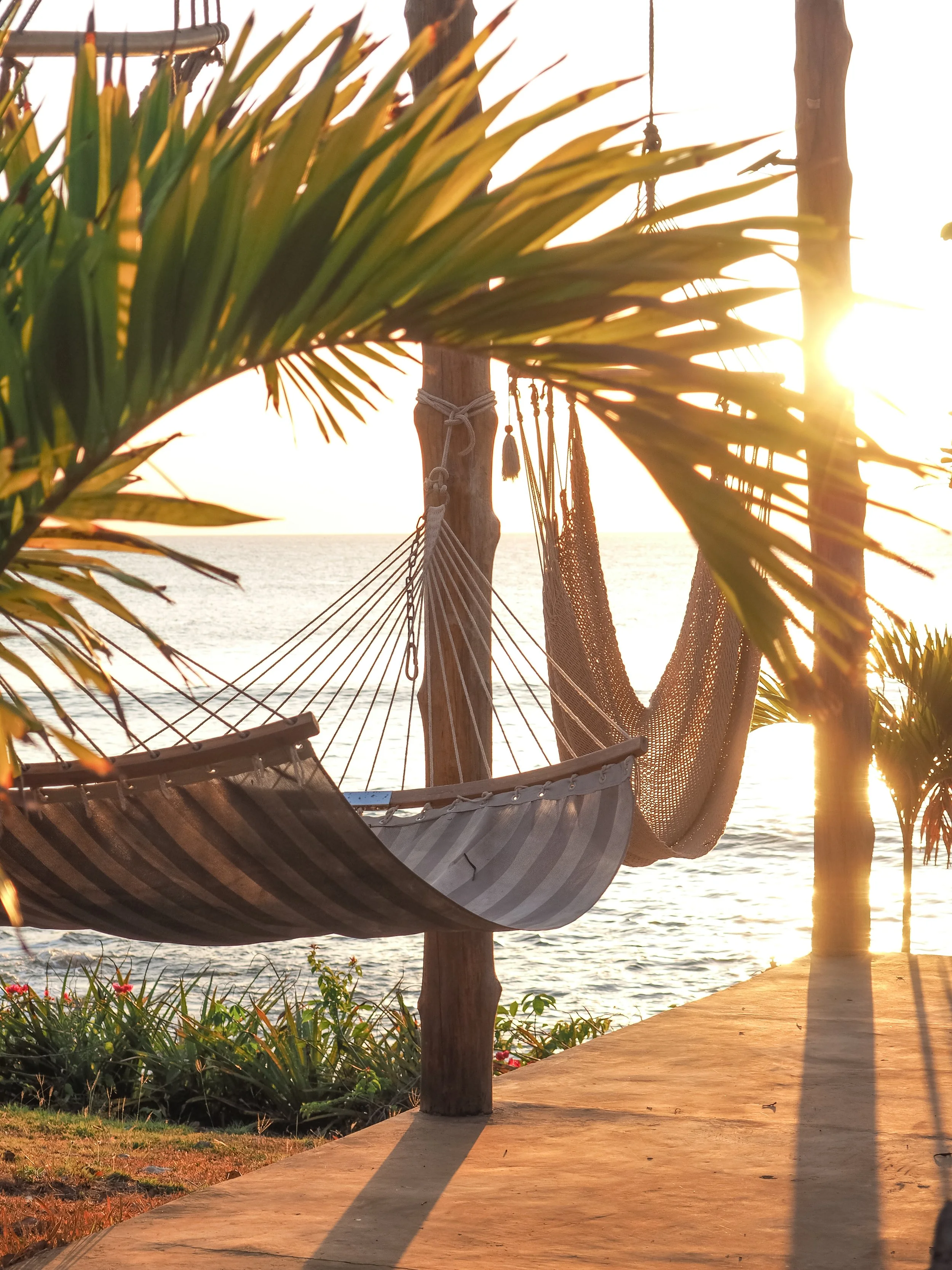 Woven hammock strung between posts glowing at golden hour beside the ocean at a Nicaragua surf and yoga retreat