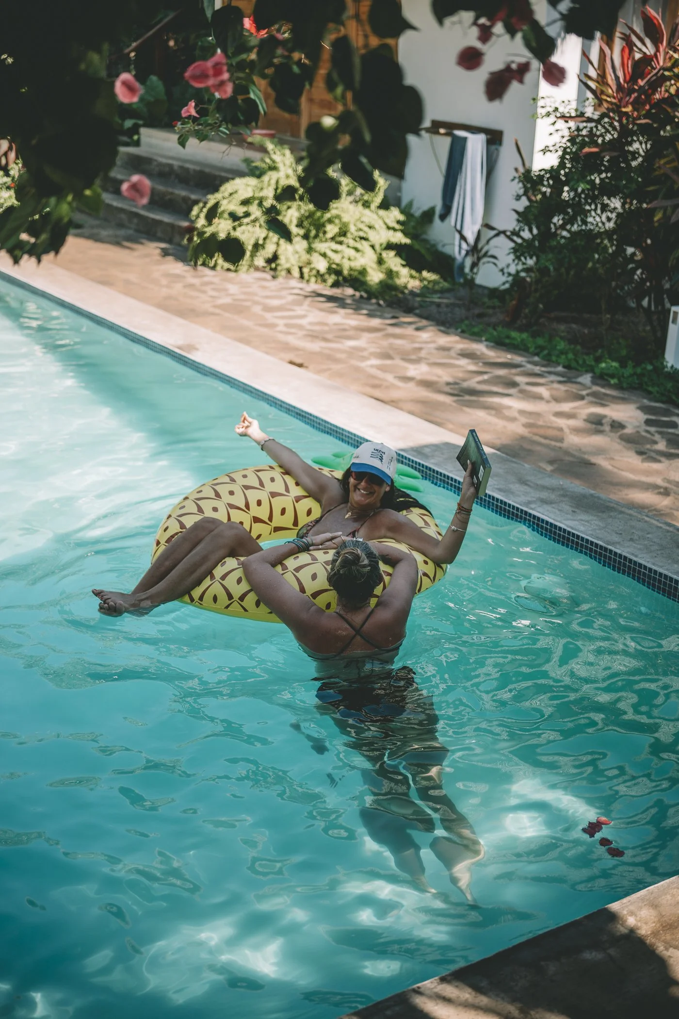 Two retreat guests laughing on a pineapple float in the pool at Still Salty Escape surf and yoga retreat in Nicaragua