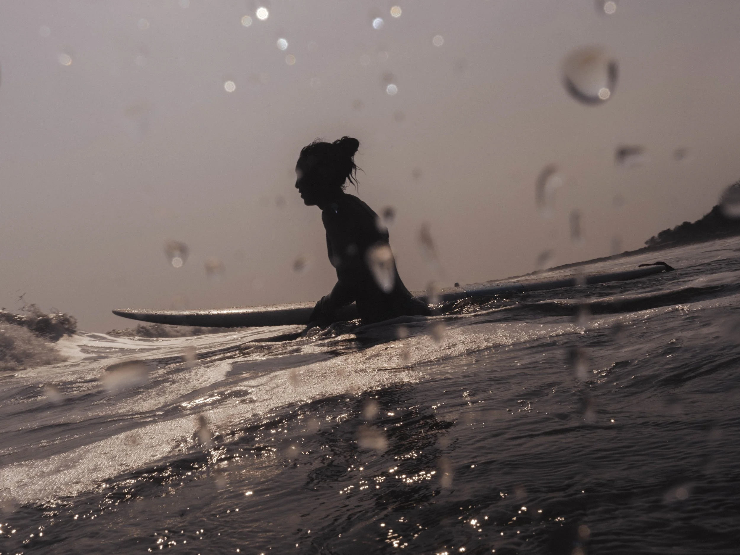 silhouette of a woman sitting on her longboard at golden hour at a surf retreat in Nicaragua