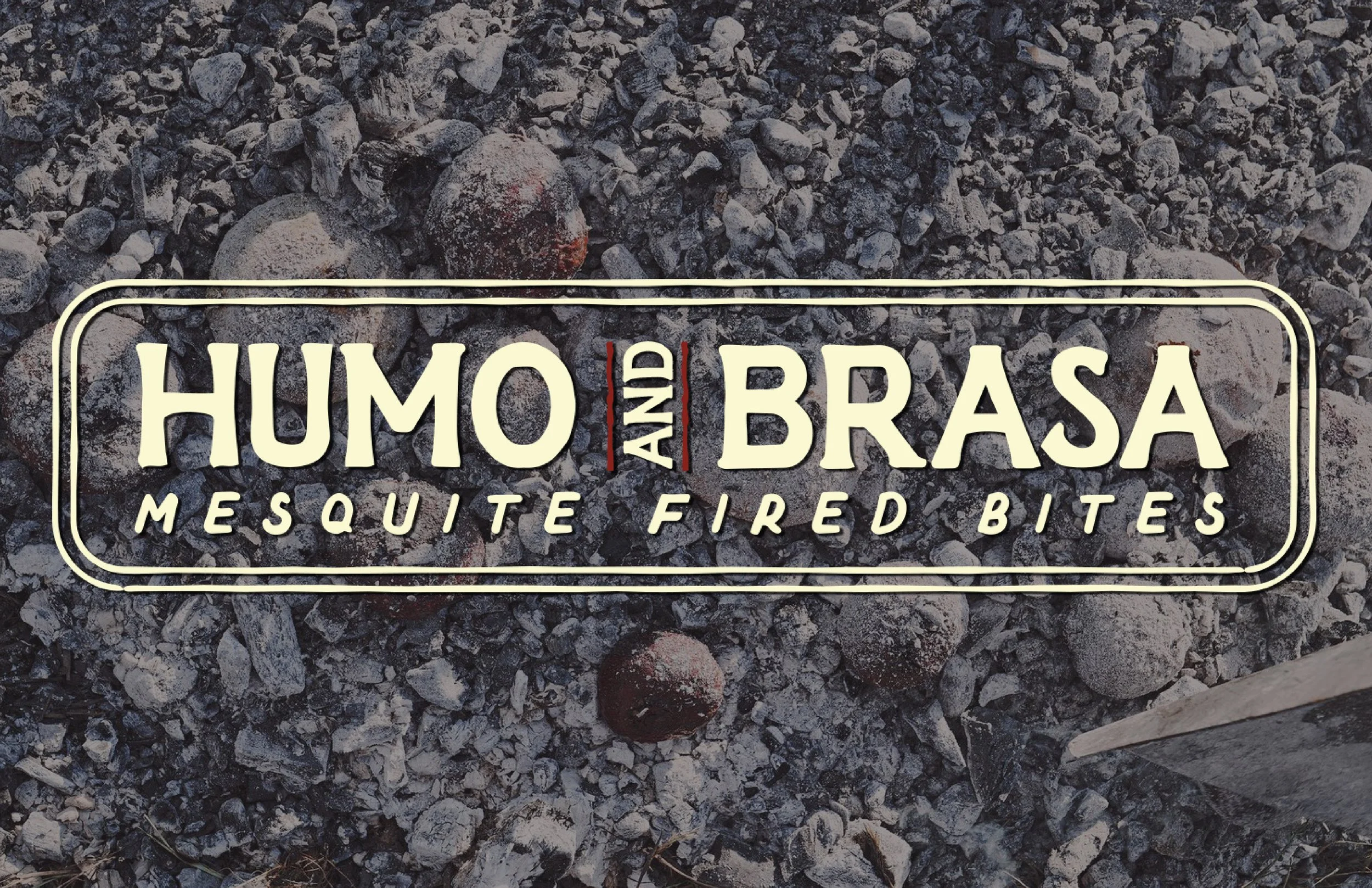 Sign with the text 'Humo and Brasa, Mesquite Fired Bites' over rocks and ashes, with some charcoal balls and a small part of a knife visible.