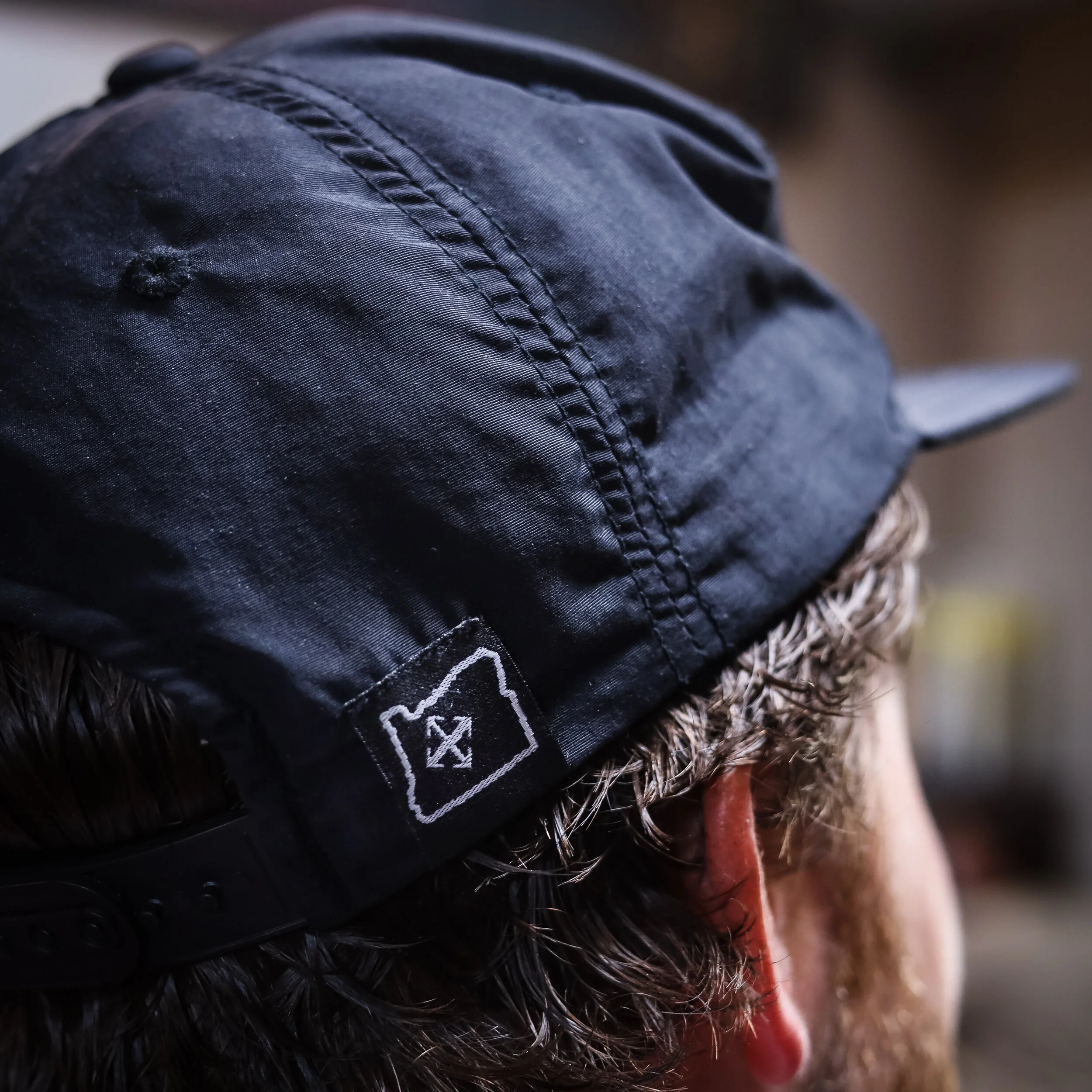Back of a person with curly hair wearing a black cap with a laundry symbol on it.