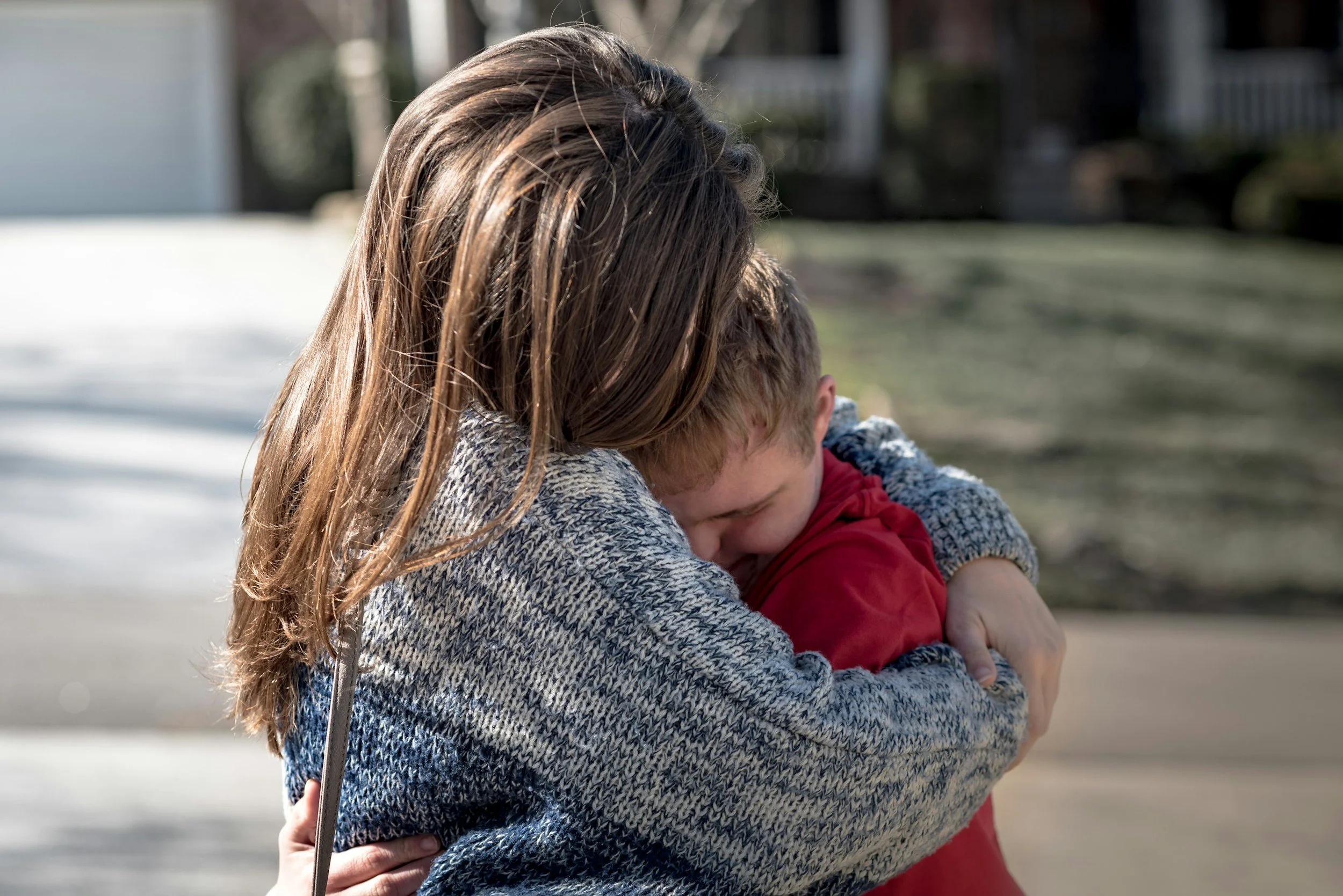 mom hugs her son outside their home