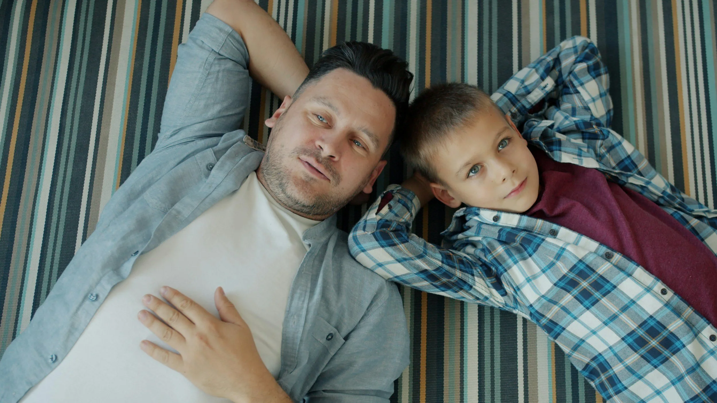 dad lays on ground with son - head to head. both are looking up