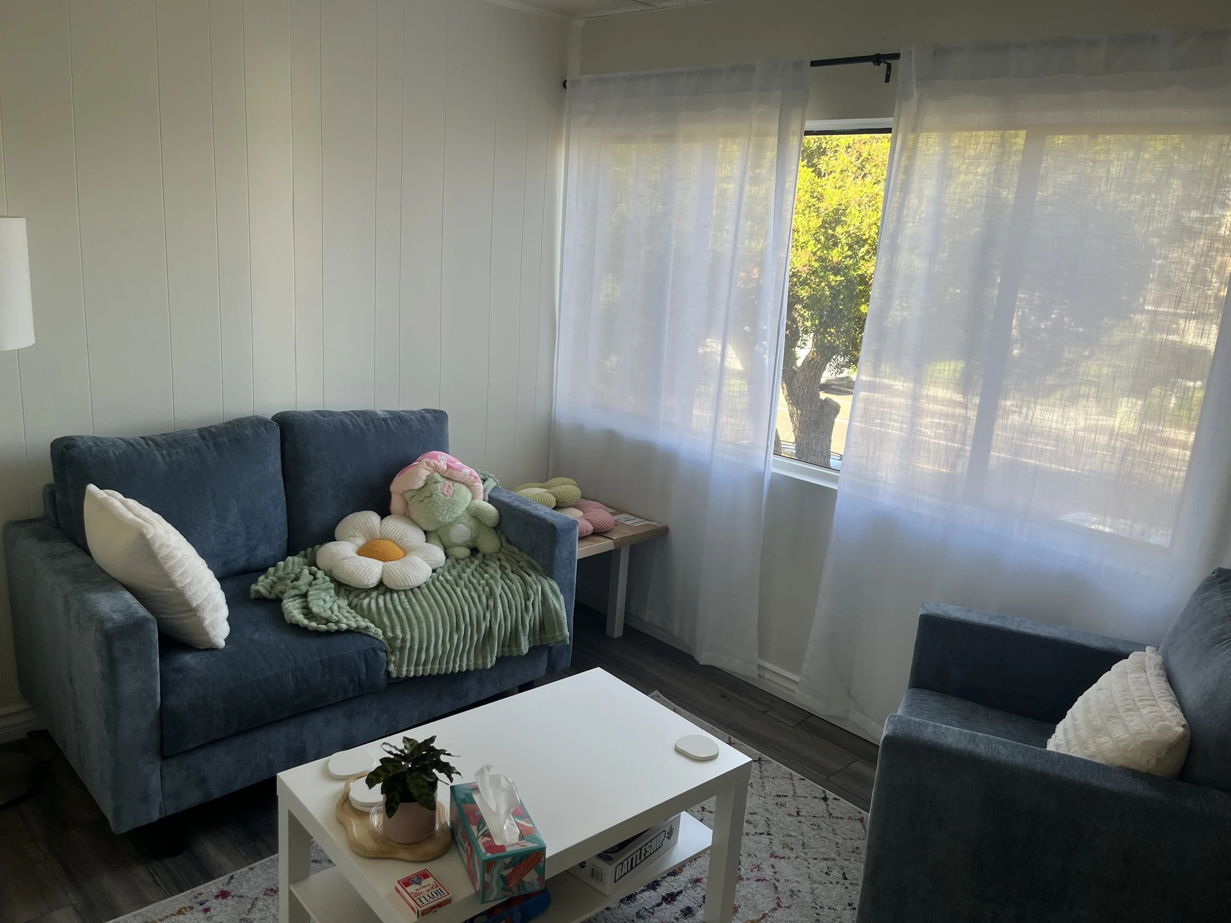 Therapist chair is seated across from couch that has pillows and blankets on it. 