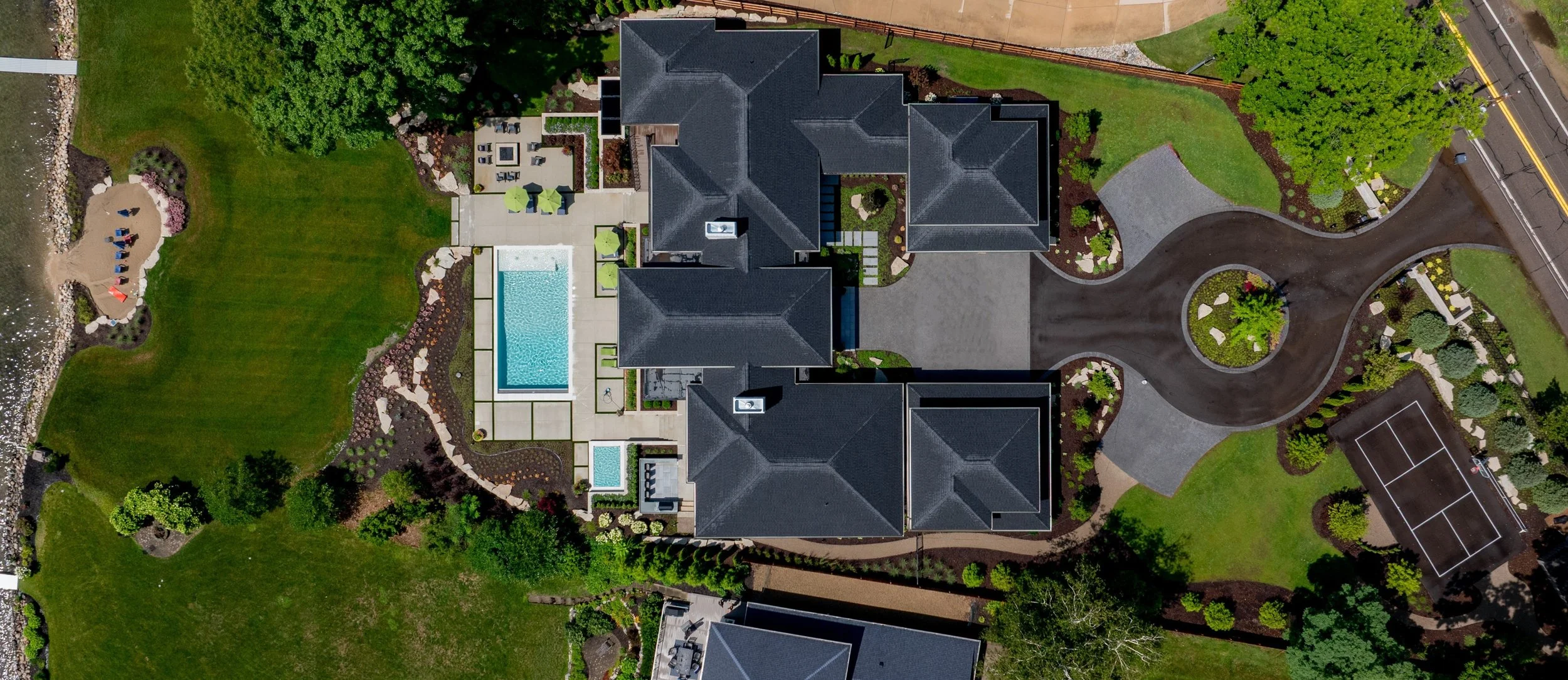 Aerial view of a large residential complex with dark gray roofs, a swimming pool, a tennis court, and landscaped gardens.