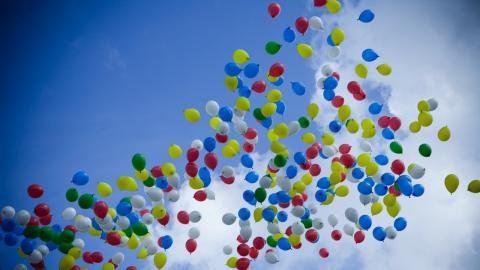 many balloons of many colours floating in a blue sky