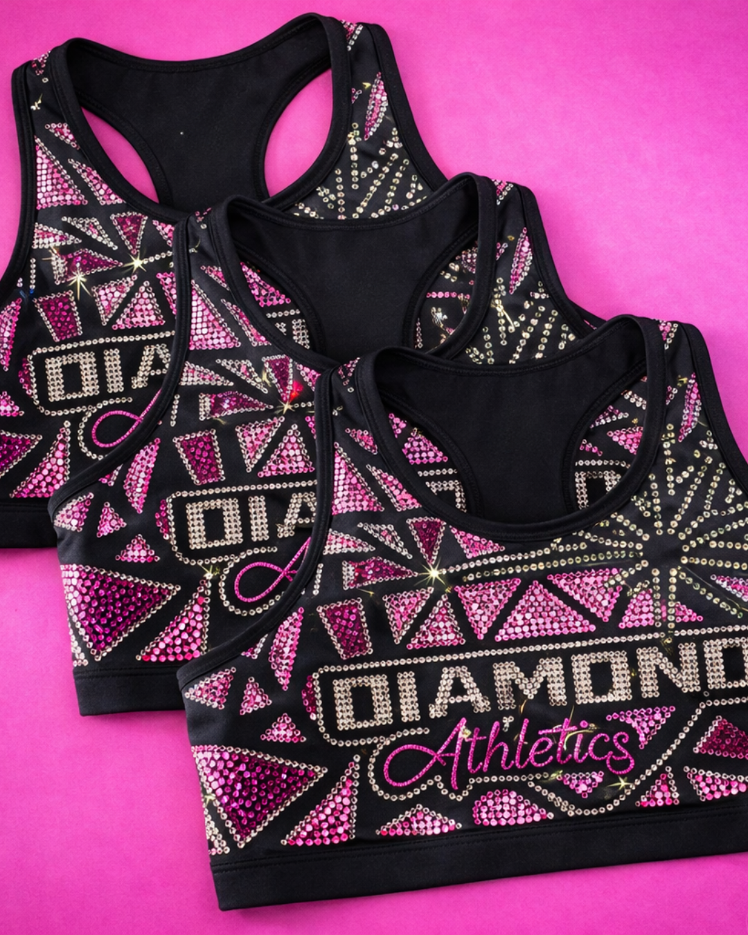 Three black sports bras with colorful rhinestone designs and the words "Diamonds Athletics" on a pink background.